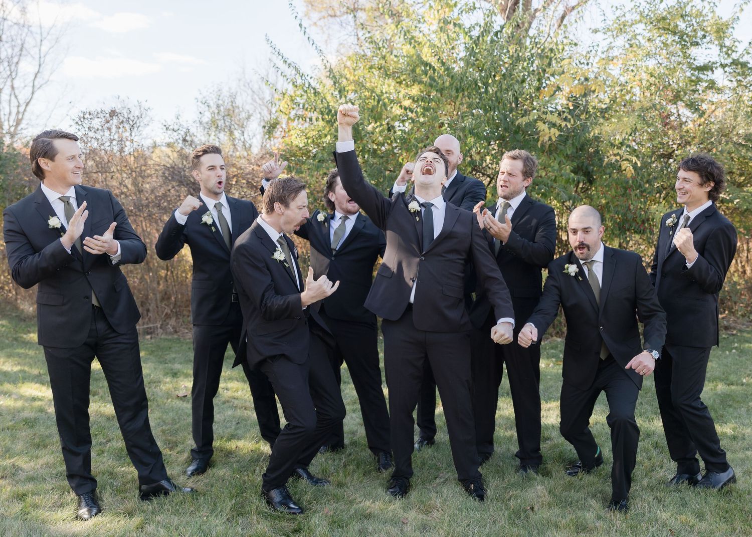 Groomsmen in black suits share candid laughing moment during outdoor wedding photoshoot.