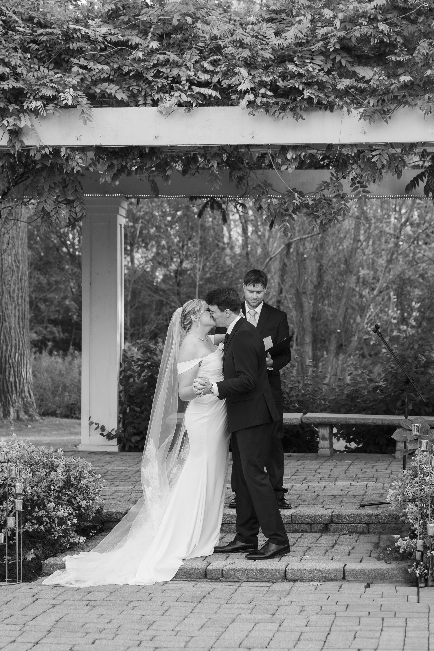 Black and white photo of wedding ceremony under garden pergola with natural light.
