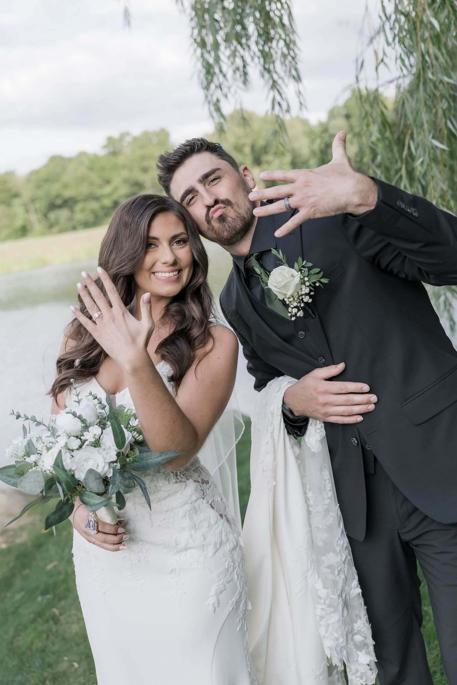 A newlywed couple shares joyful candid moments by a lakeside with willow trees in the background.