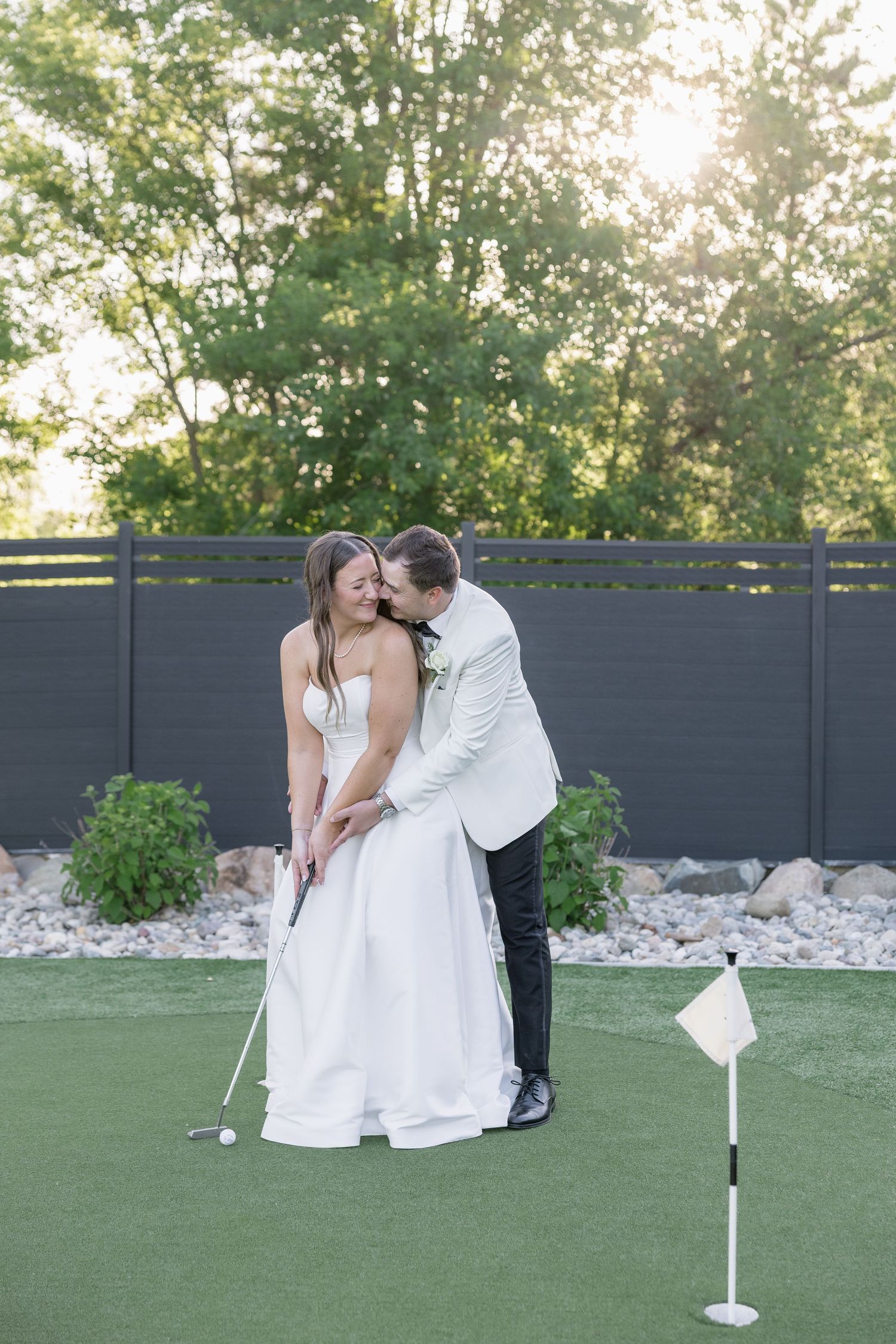 Bride and groom share a romantic moment on a putting green, with the groom helping the bride putt on their wedding day.