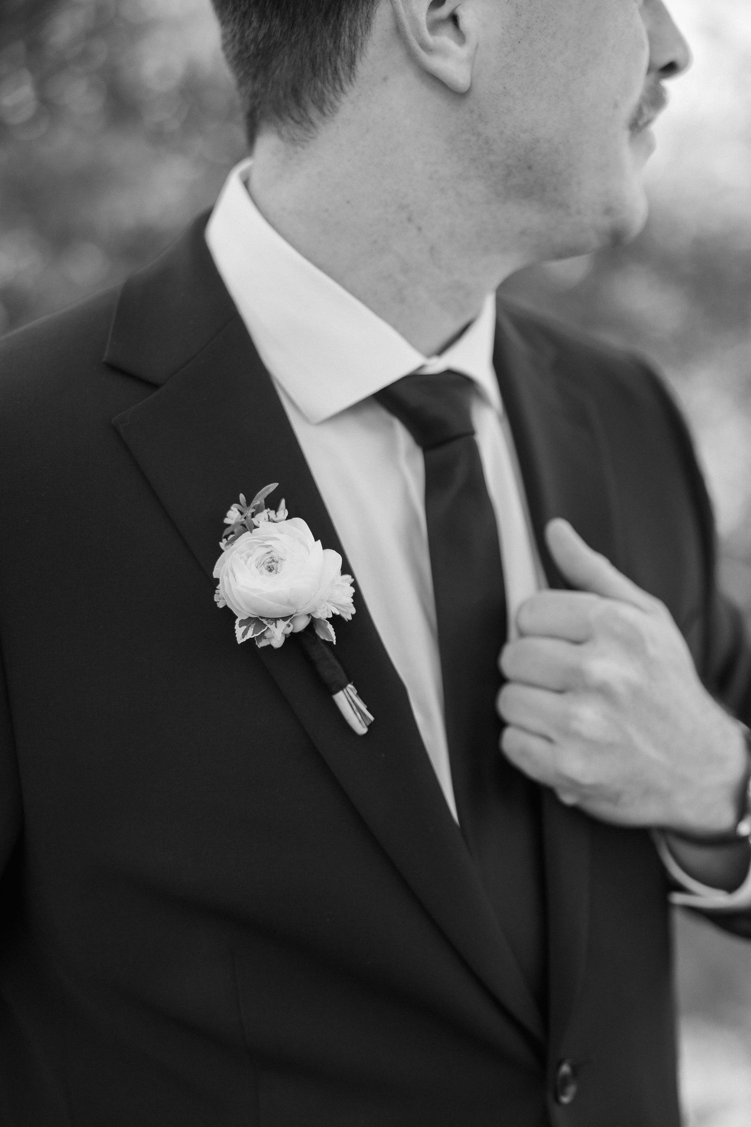 Black and white detail shot of boutonniere and suit lapel with elegant white flower.