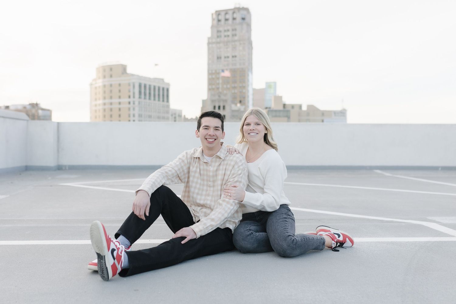 A couple sitting casually on a rooftop with city skyline in soft lighting.