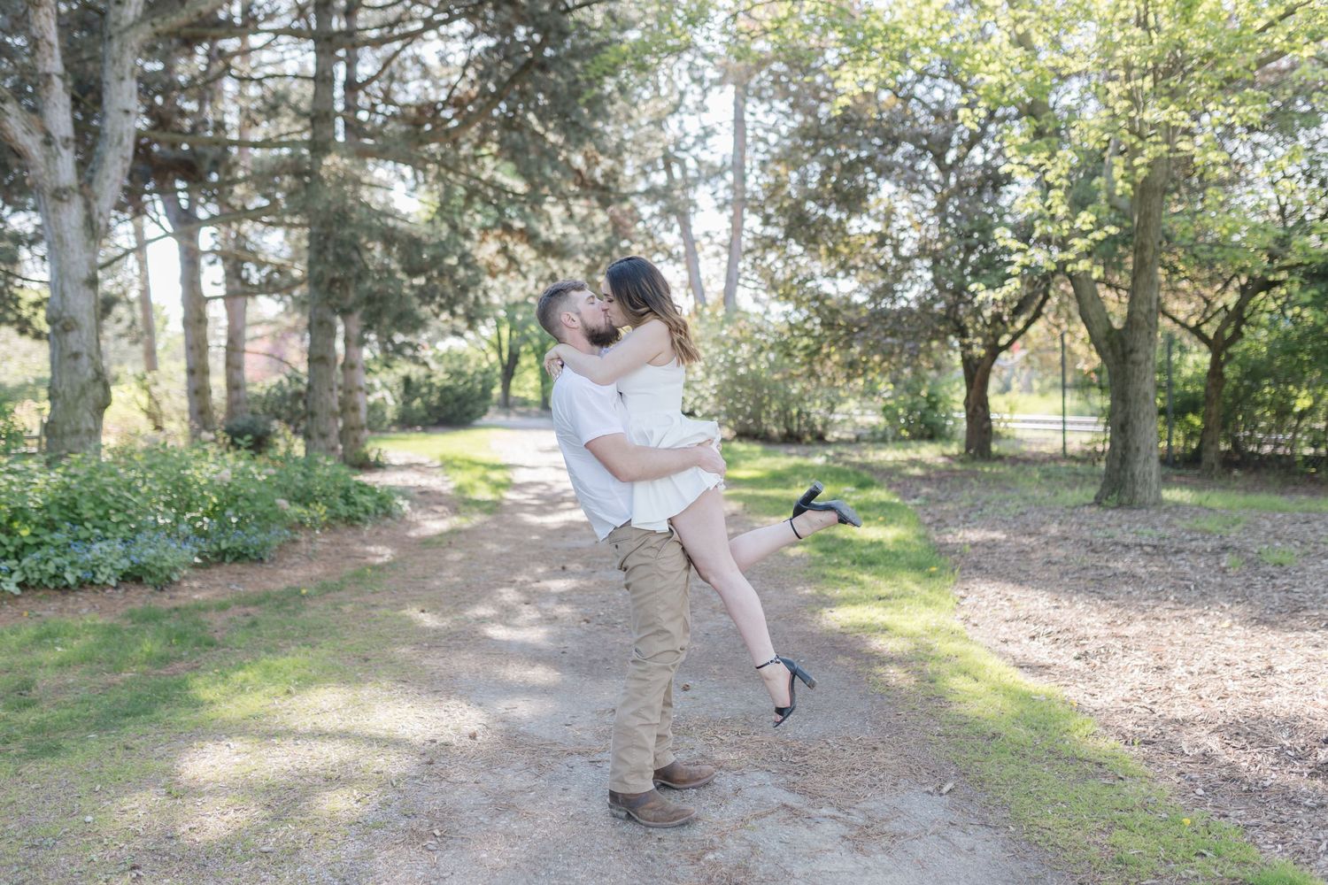 Romantic couple shares a playful embrace on a sunlit forest path.