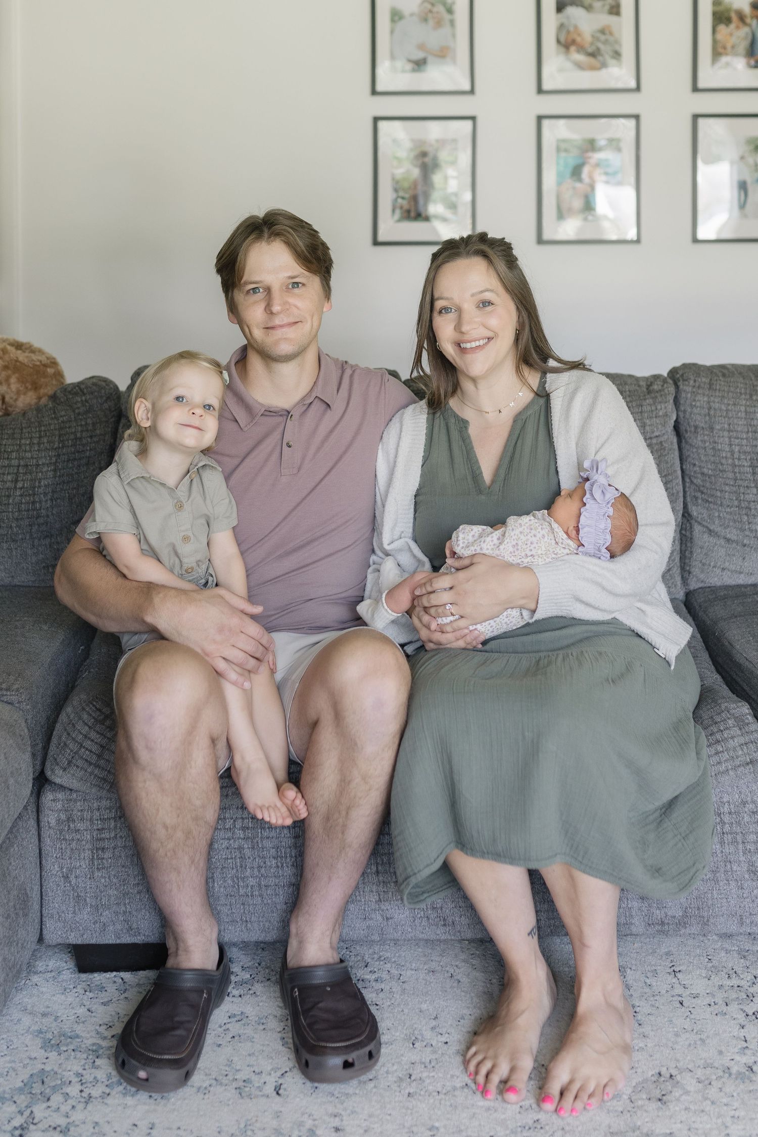 Family sitting together on a gray couch in a modern living room with framed artwork on the wall.