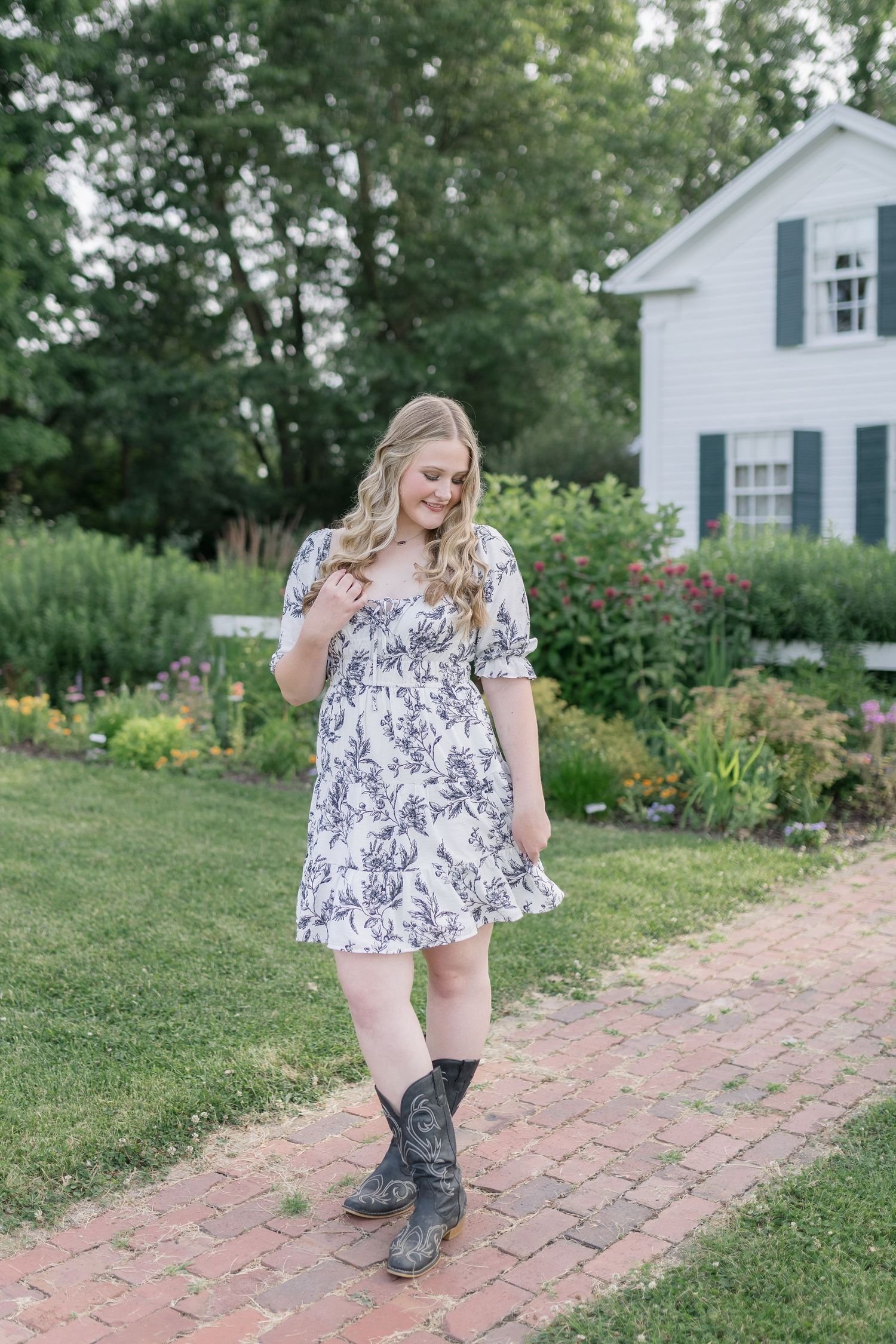 Country-style fashion shoot on a brick pathway with floral dress and western boots in a garden setting.