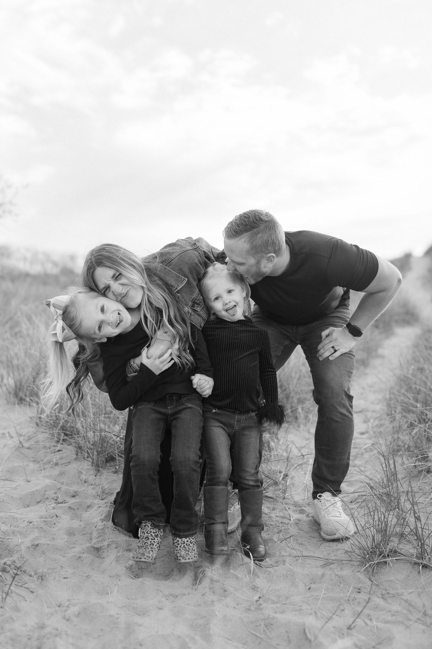 A black and white photo series shows a playful group in dark clothing leaning and posing together on a grassy hillside.