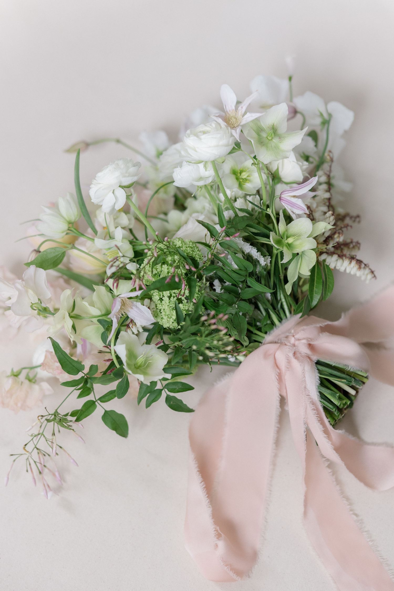 Delicate floral arrangement with white blooms and greenery tied with pink silk ribbon.