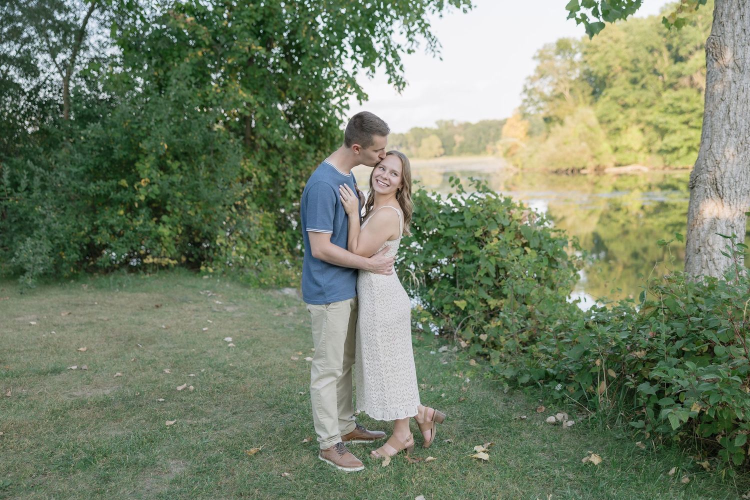 A couple embraces in a romantic outdoor photoshoot surrounded by lush greenery and natural sunlight.