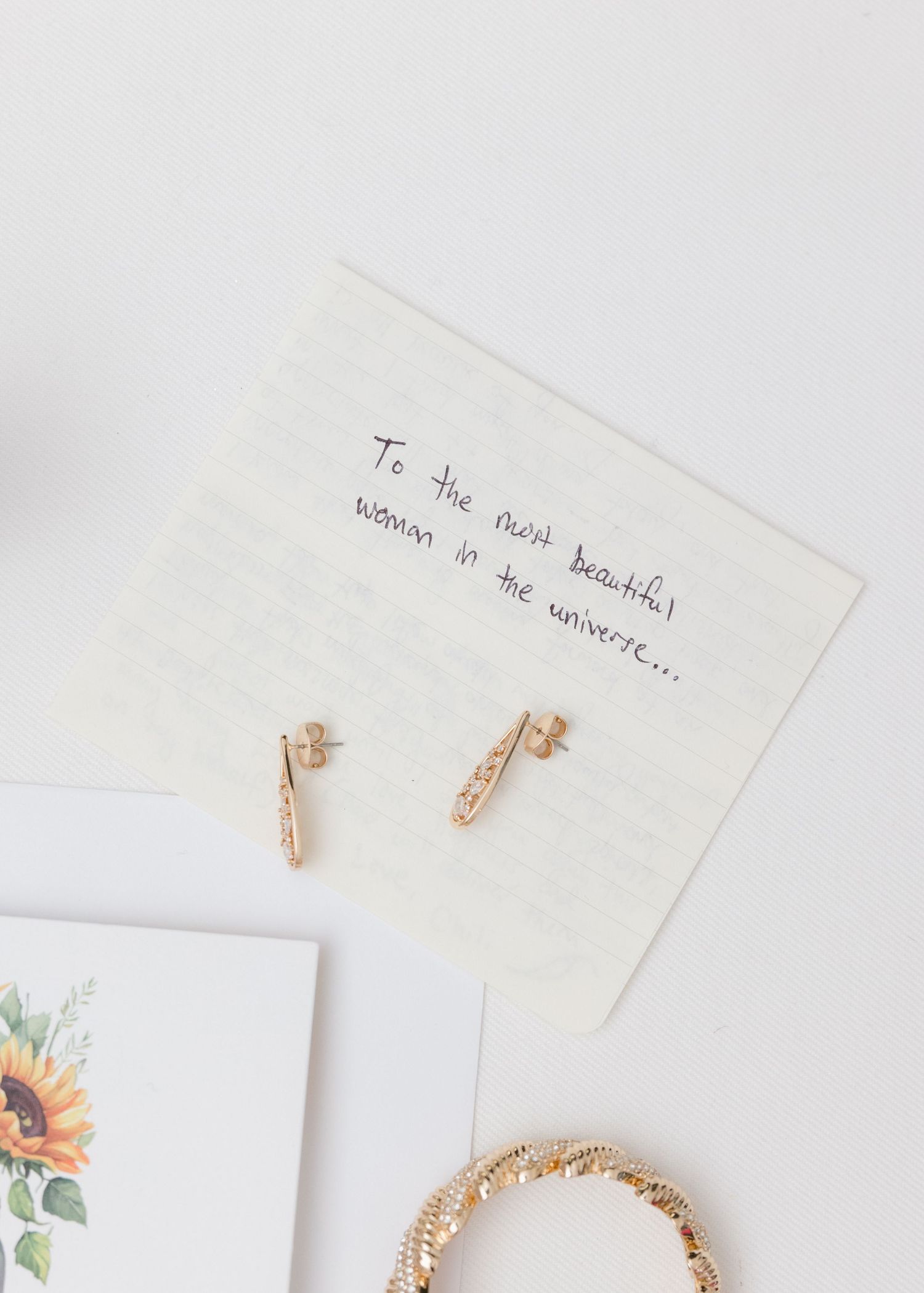 Wedding details flat lay with handwritten note, earrings and floral invitation.