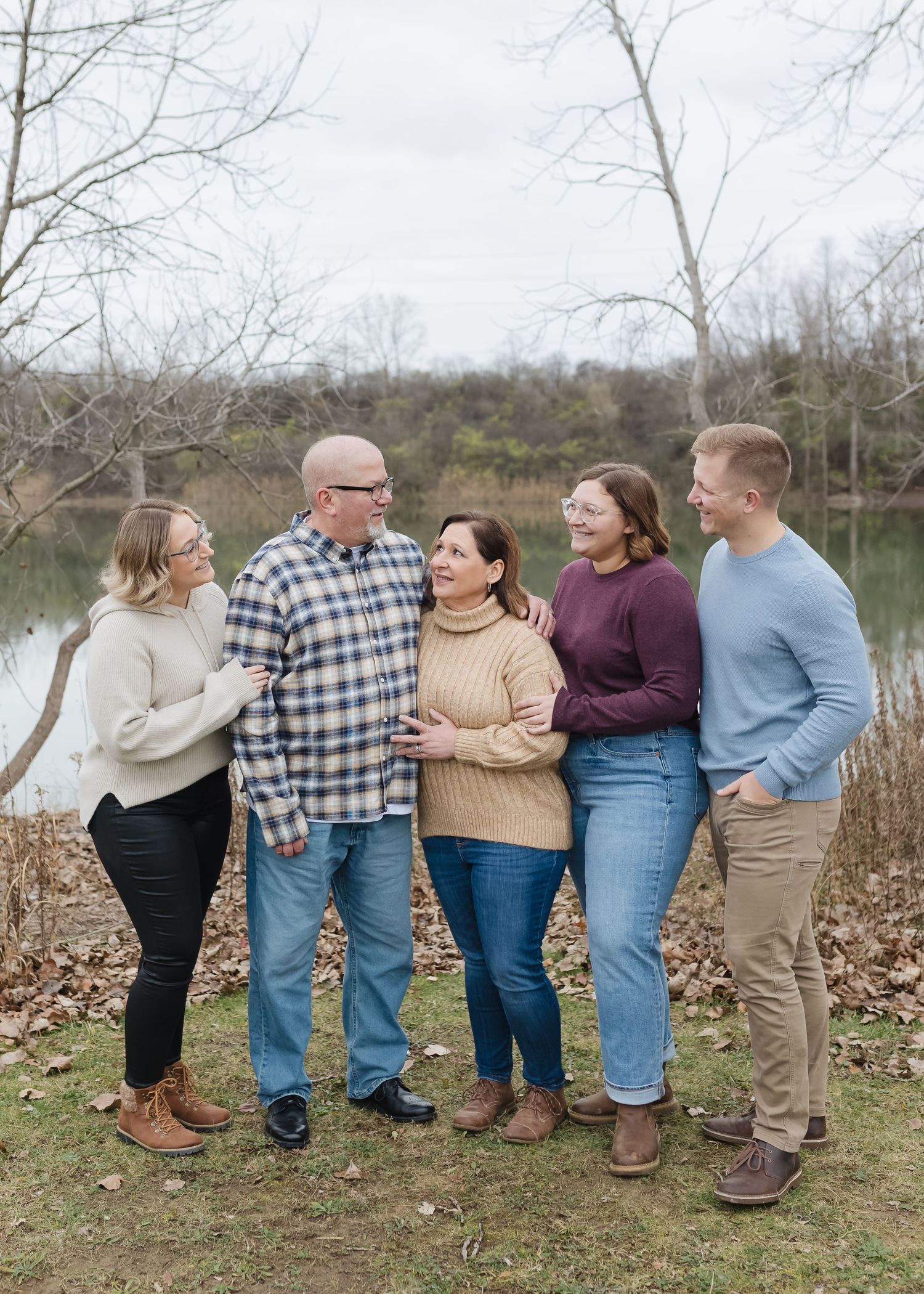 Group of five people in casual sweaters standing together by a lake on an autumn day.