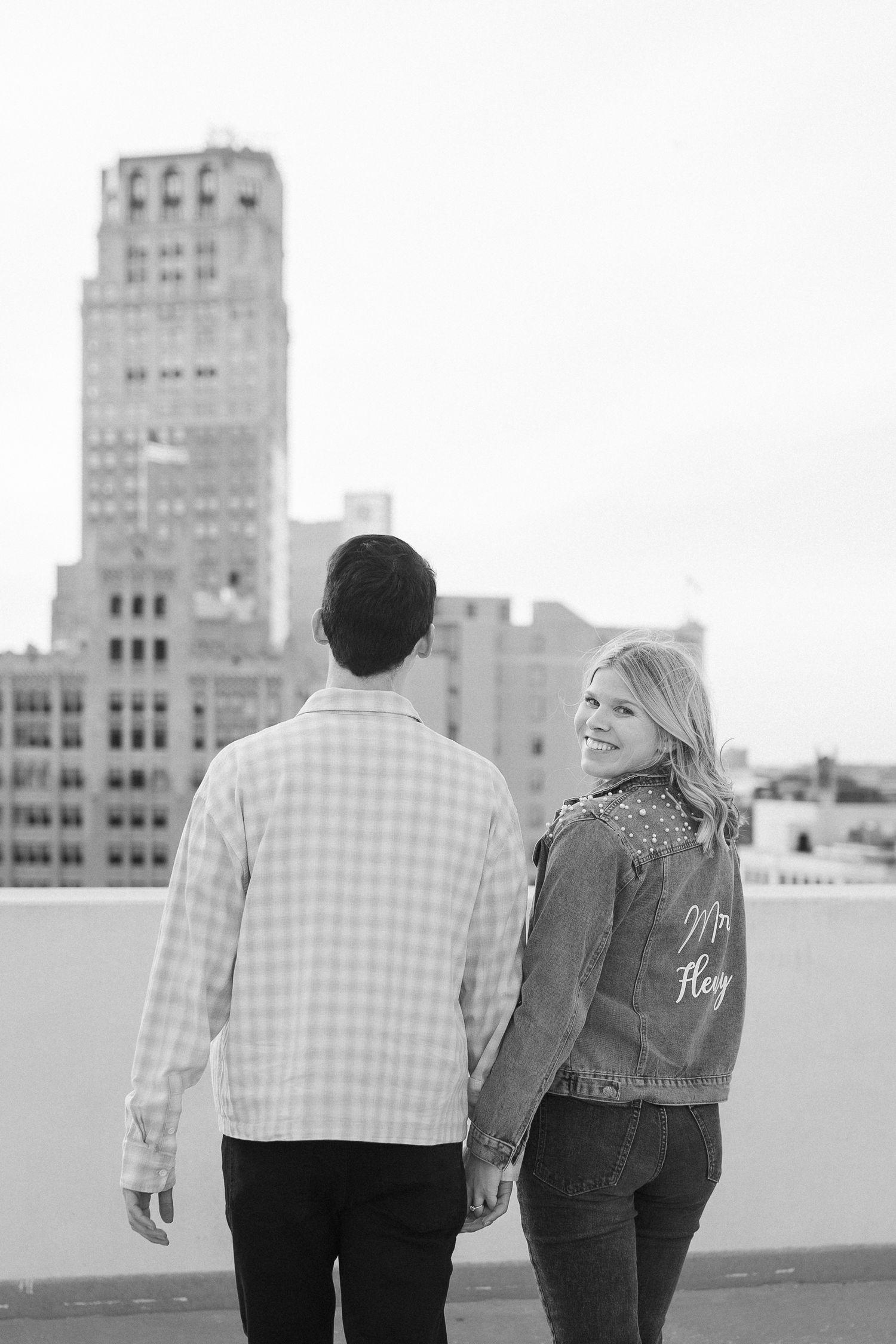Black and white photo of couple on urban rooftop with art deco building in background.
