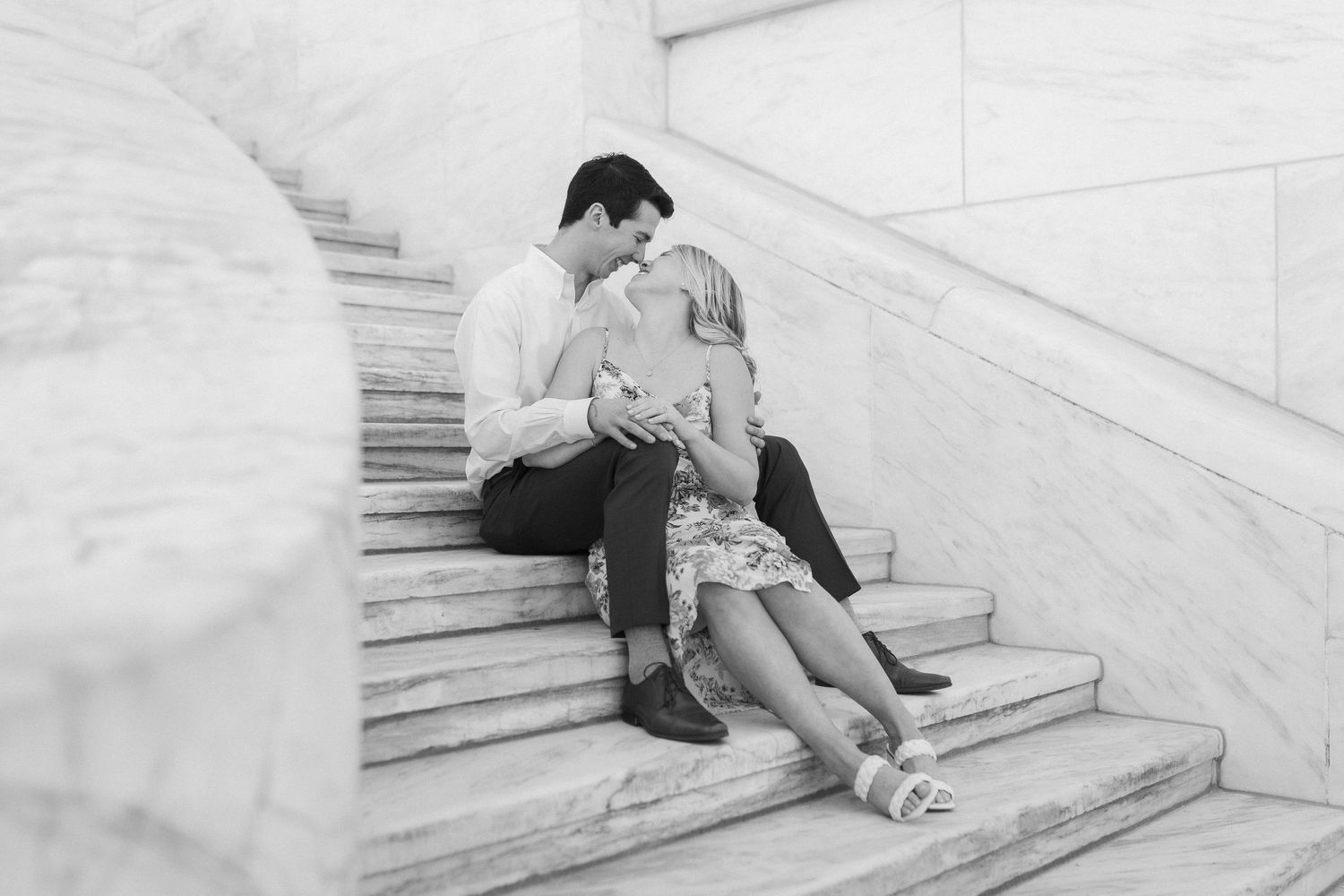A romantic black and white photo of a couple sitting and embracing on white marble stairs.