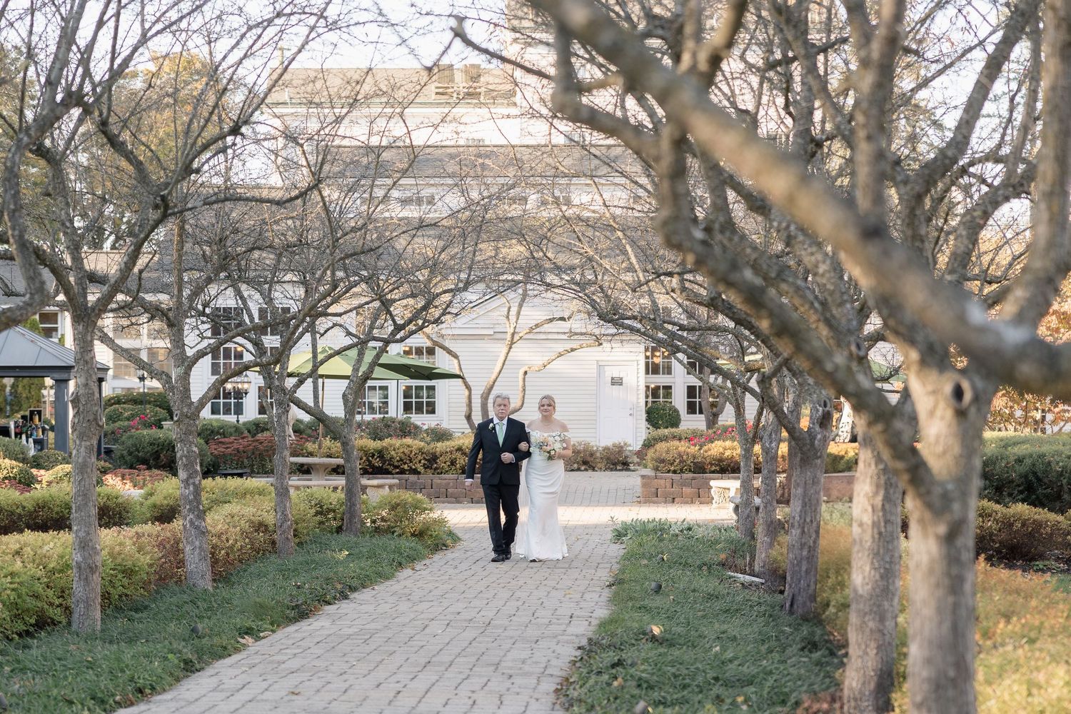 A tree-lined brick pathway leads to a wedding ceremony venue with autumn foliage.