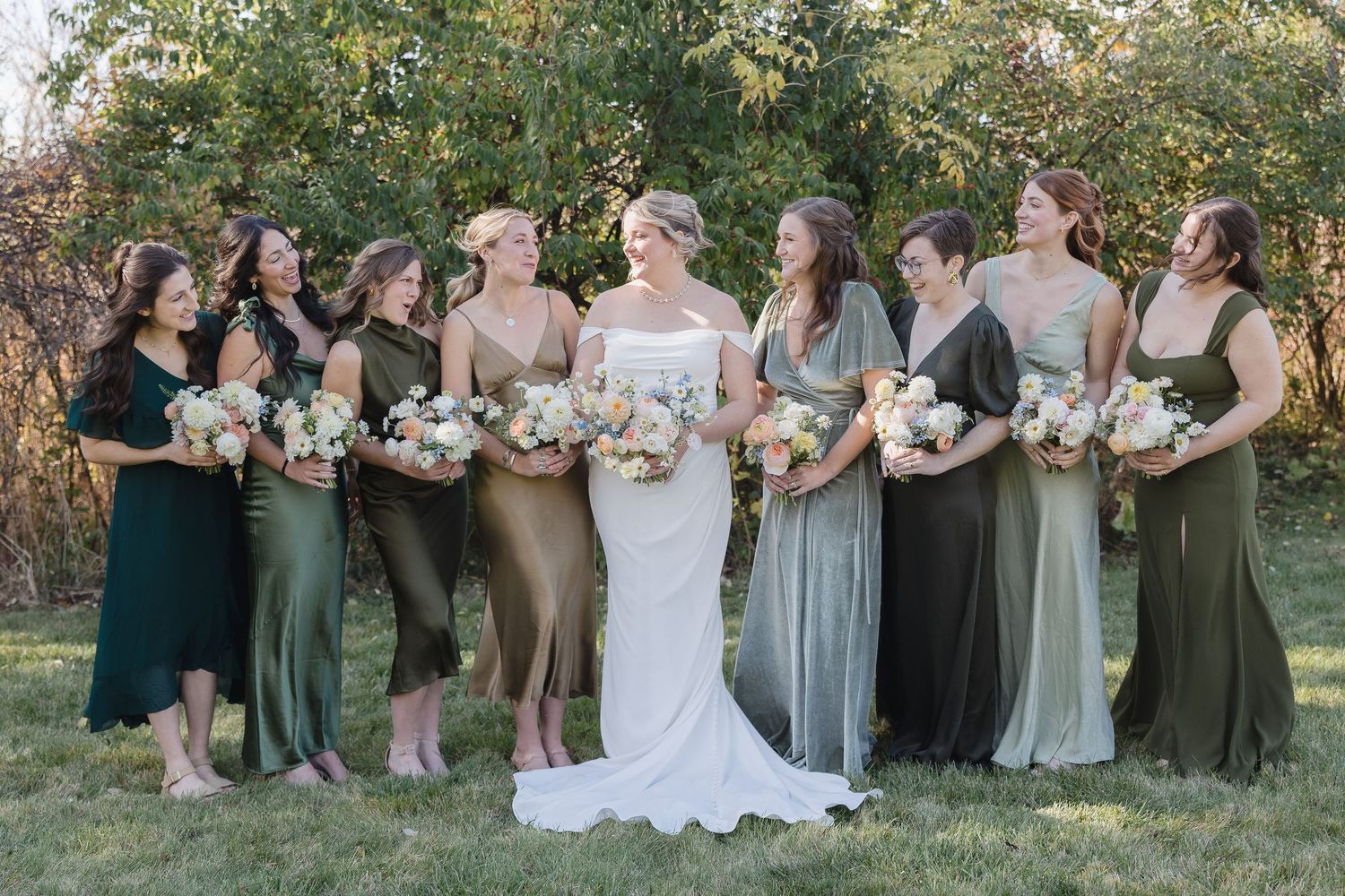 Wedding party photo featuring bridesmaids in varying shades of green dresses holding matching bouquets.