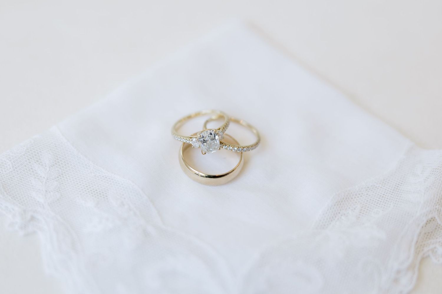 Gold wedding ring set with diamond solitaire engagement ring displayed on white lace fabric.