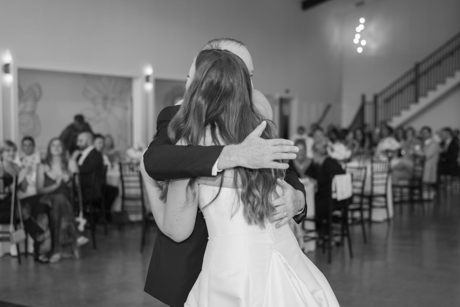 Bride and groom share emotional first dance at wedding reception in black and white photo.