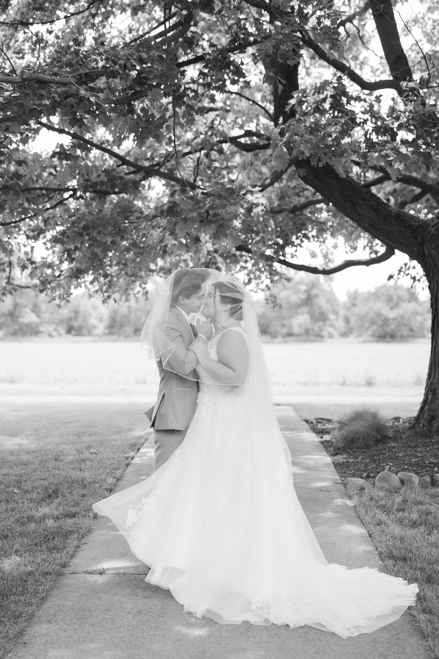 A romantic black and white wedding portrait series showing a couple dancing under a large tree in a meadow.