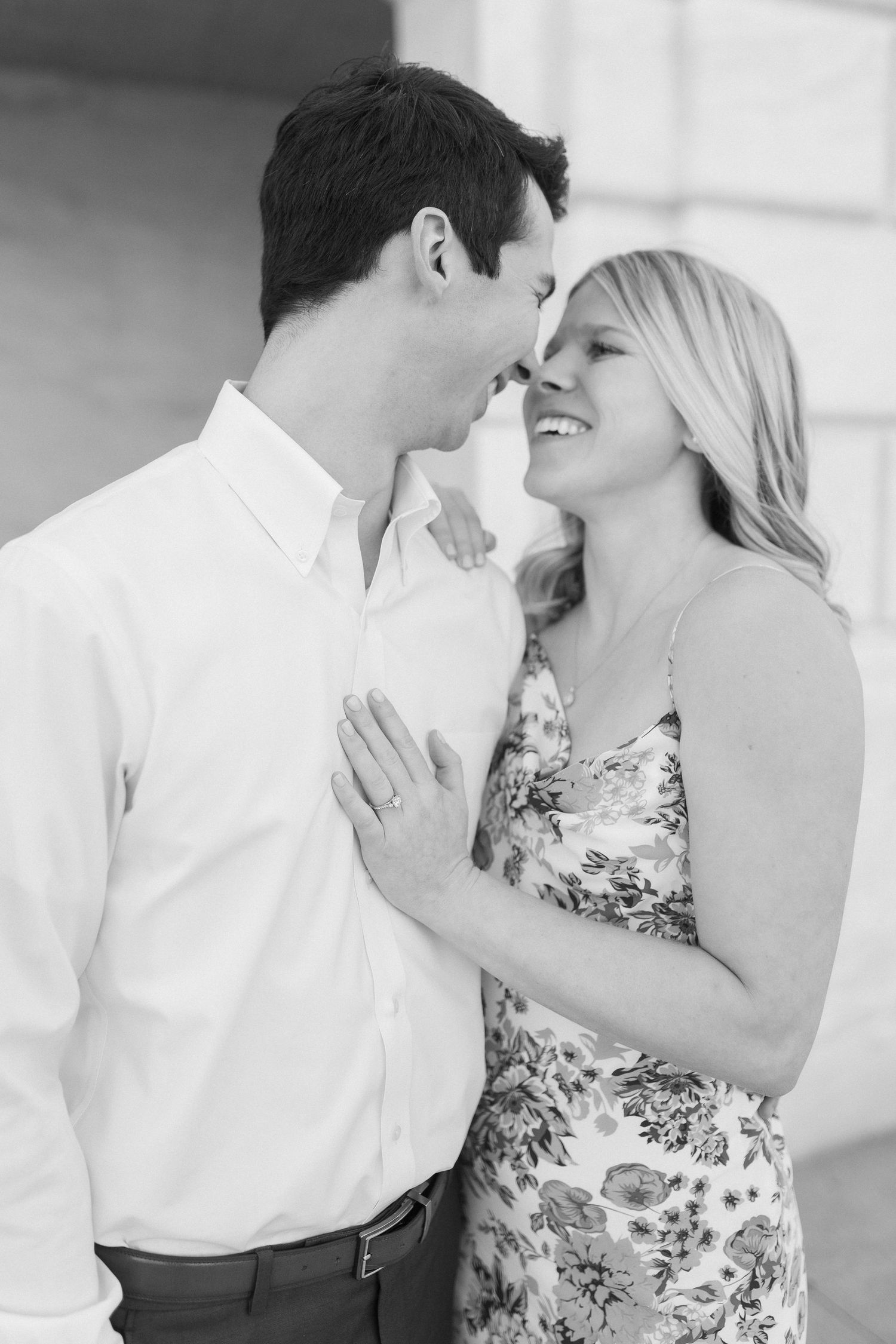 A romantic couple embraces on a bright sunny day, with her wearing a floral dress and him in a white shirt.