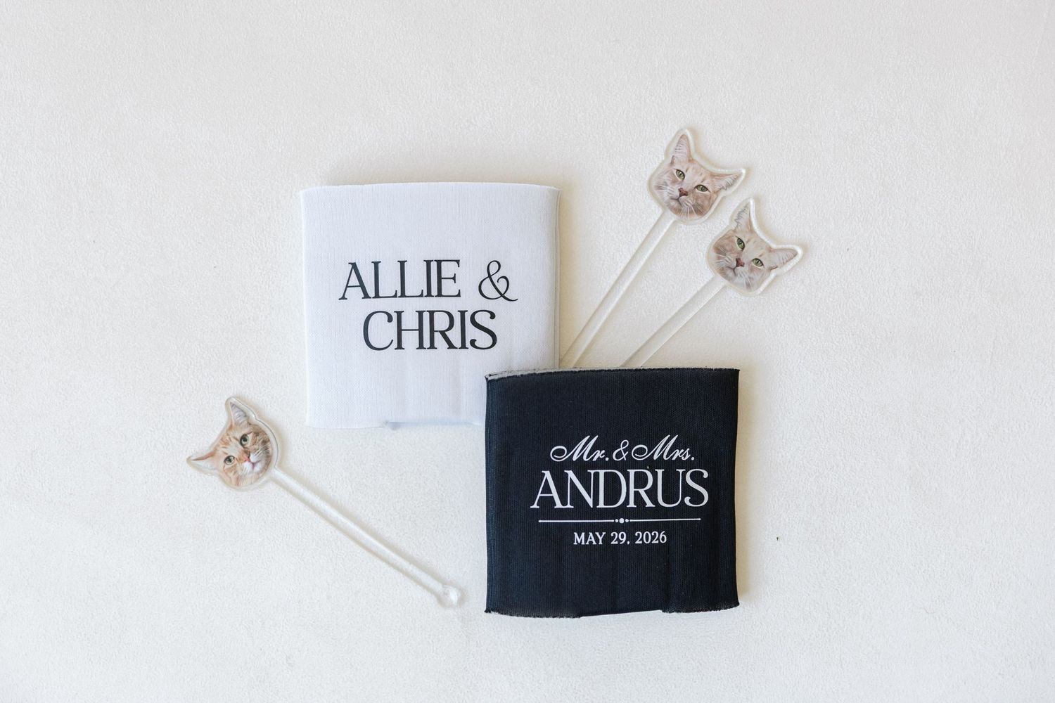 White and black personalized wedding koozies for Allie & Chris and Mr. & Mrs. Andrus with decorative cat stirrers.