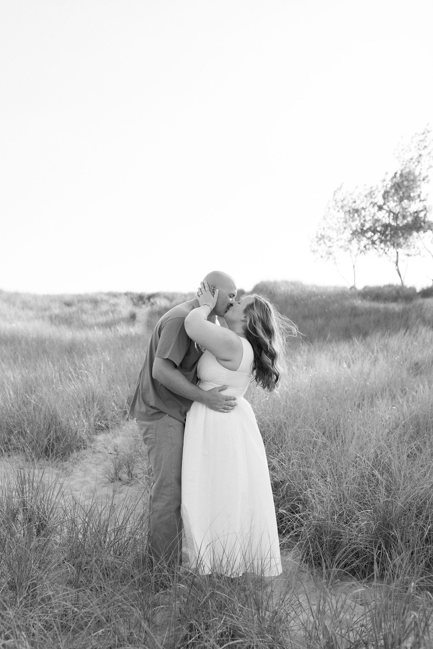 A romantic black and white photo series of a couple embracing in a serene field of tall grass.