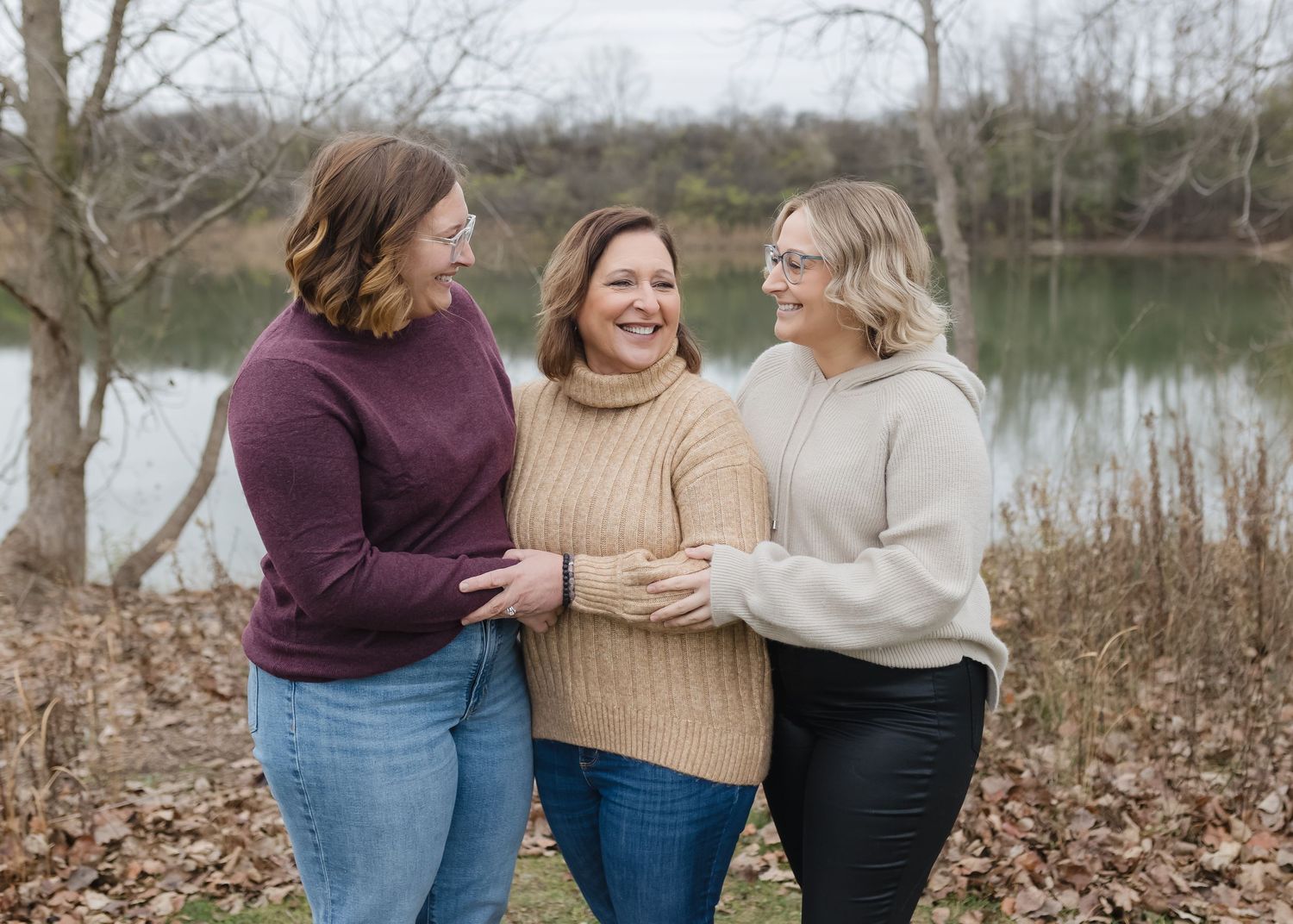Three friends walk together and embrace while enjoying a scenic autumn walk by a lake.