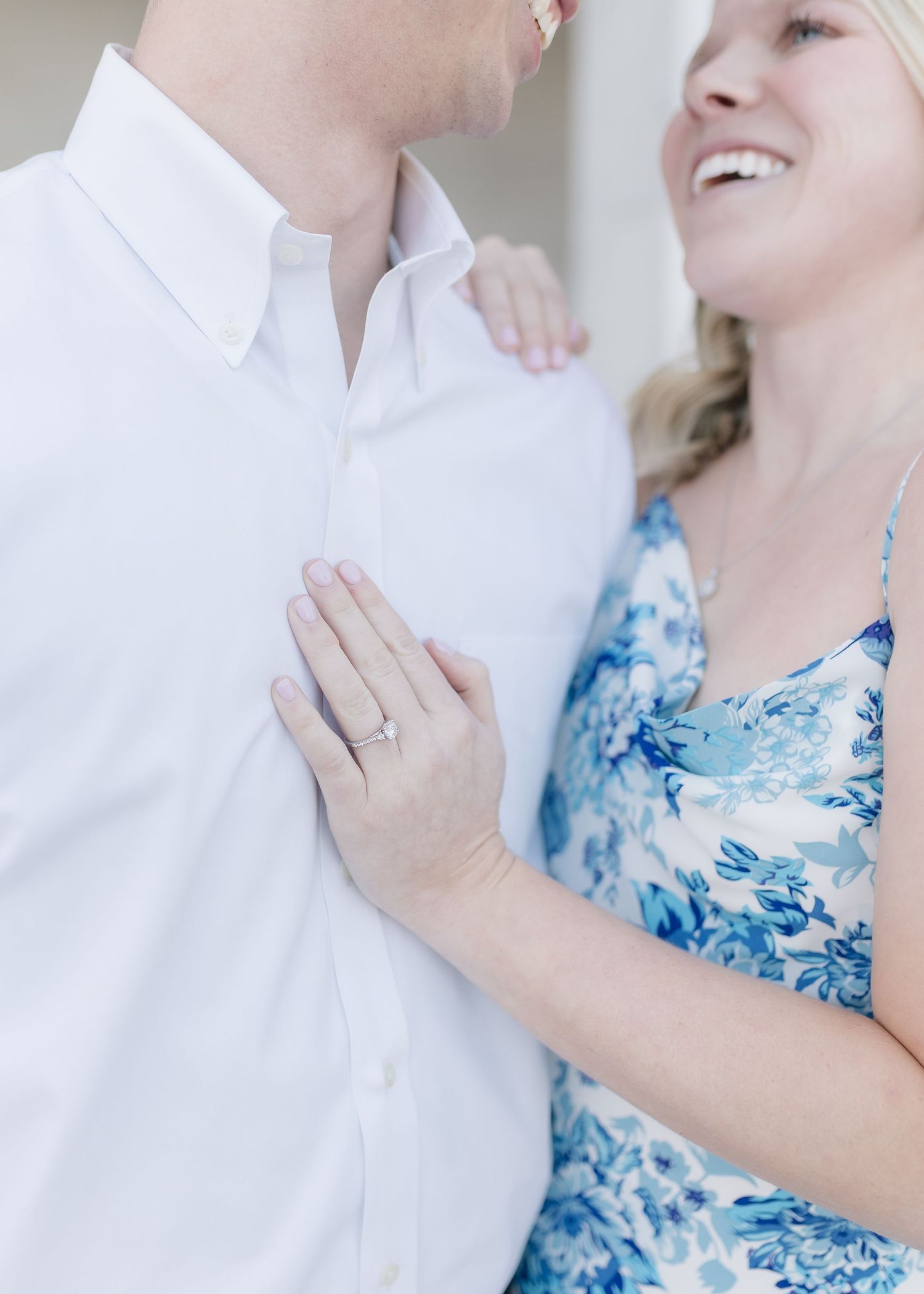A romantic engagement moment showing a sparkling ring and blue floral dress.
