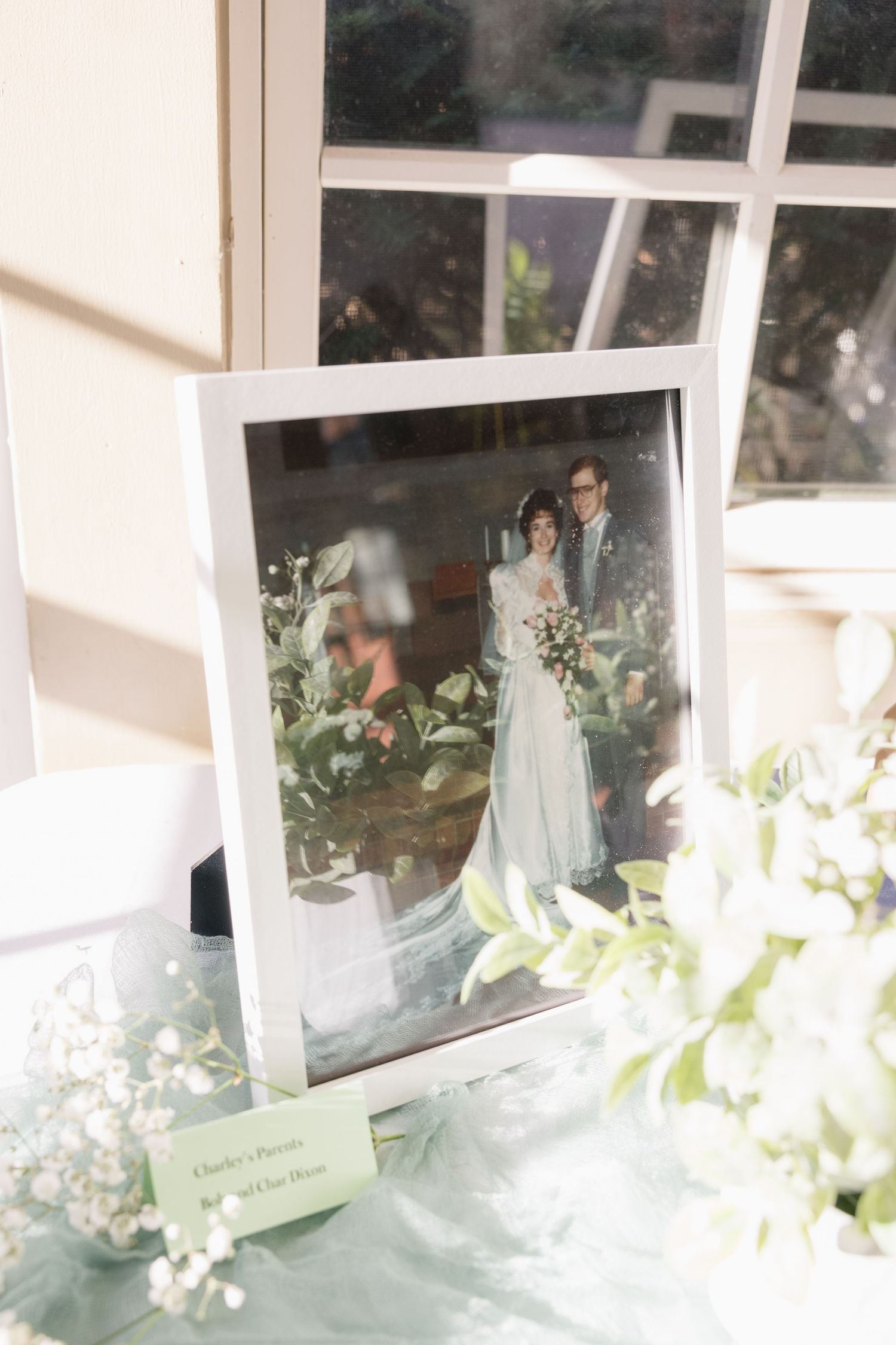 Framed wedding photo displayed among white flowers and delicate decor on a soft blue surface.