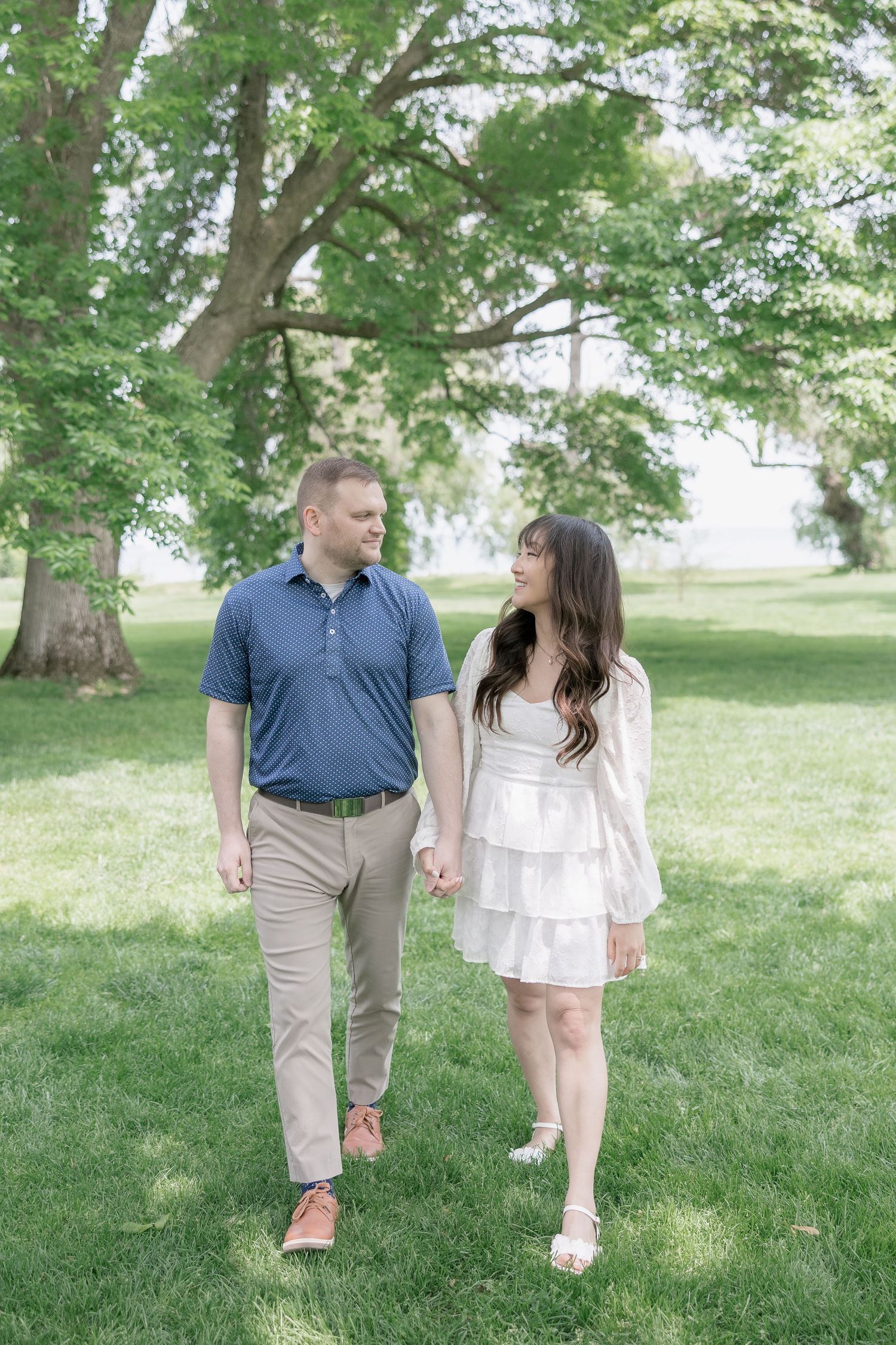 A couple walks hand in hand through a lush green park on a bright summer day wearing coordinated casual outfits.