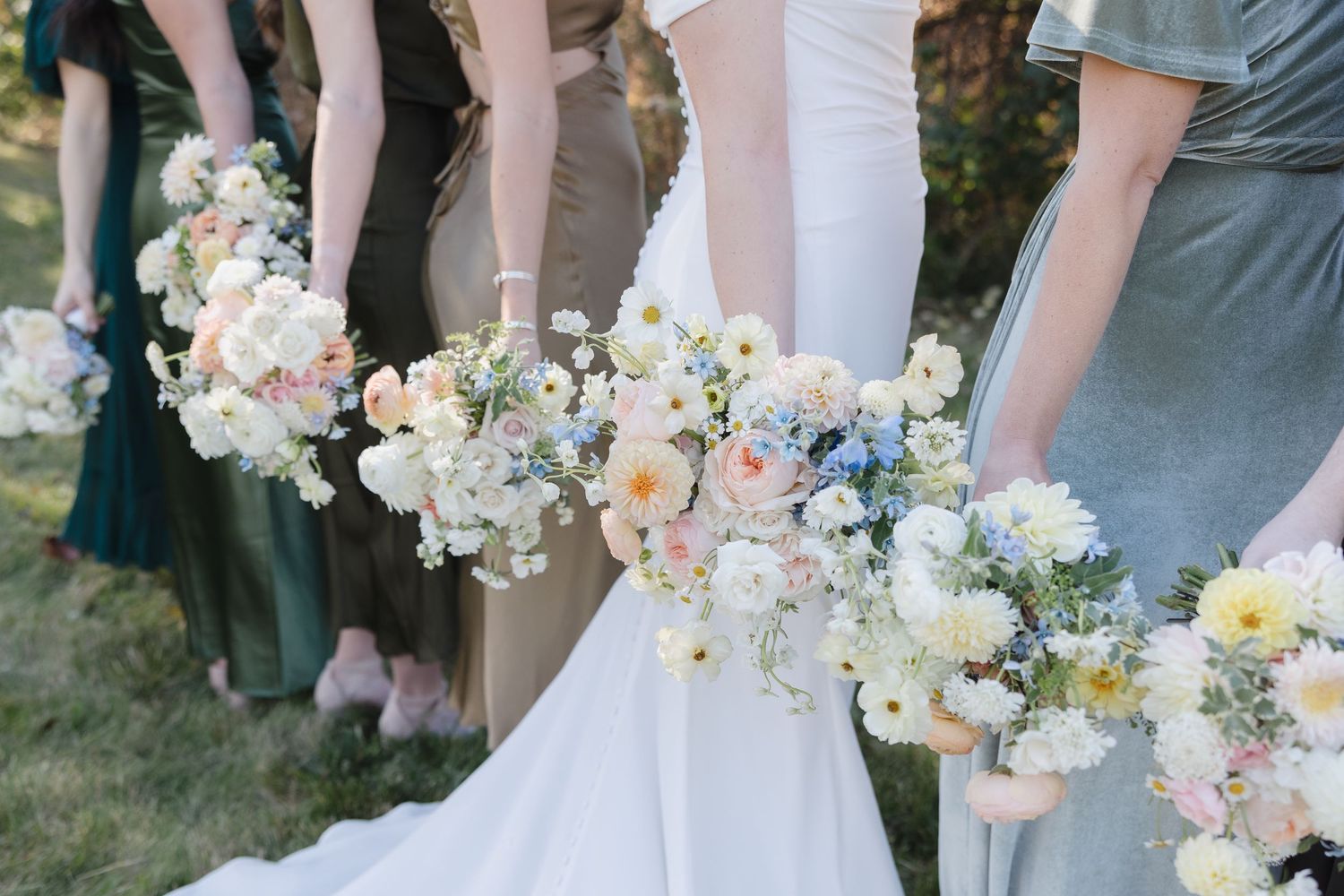 Detail shot of bridesmaids holding pastel bouquets against flowing dresses.
