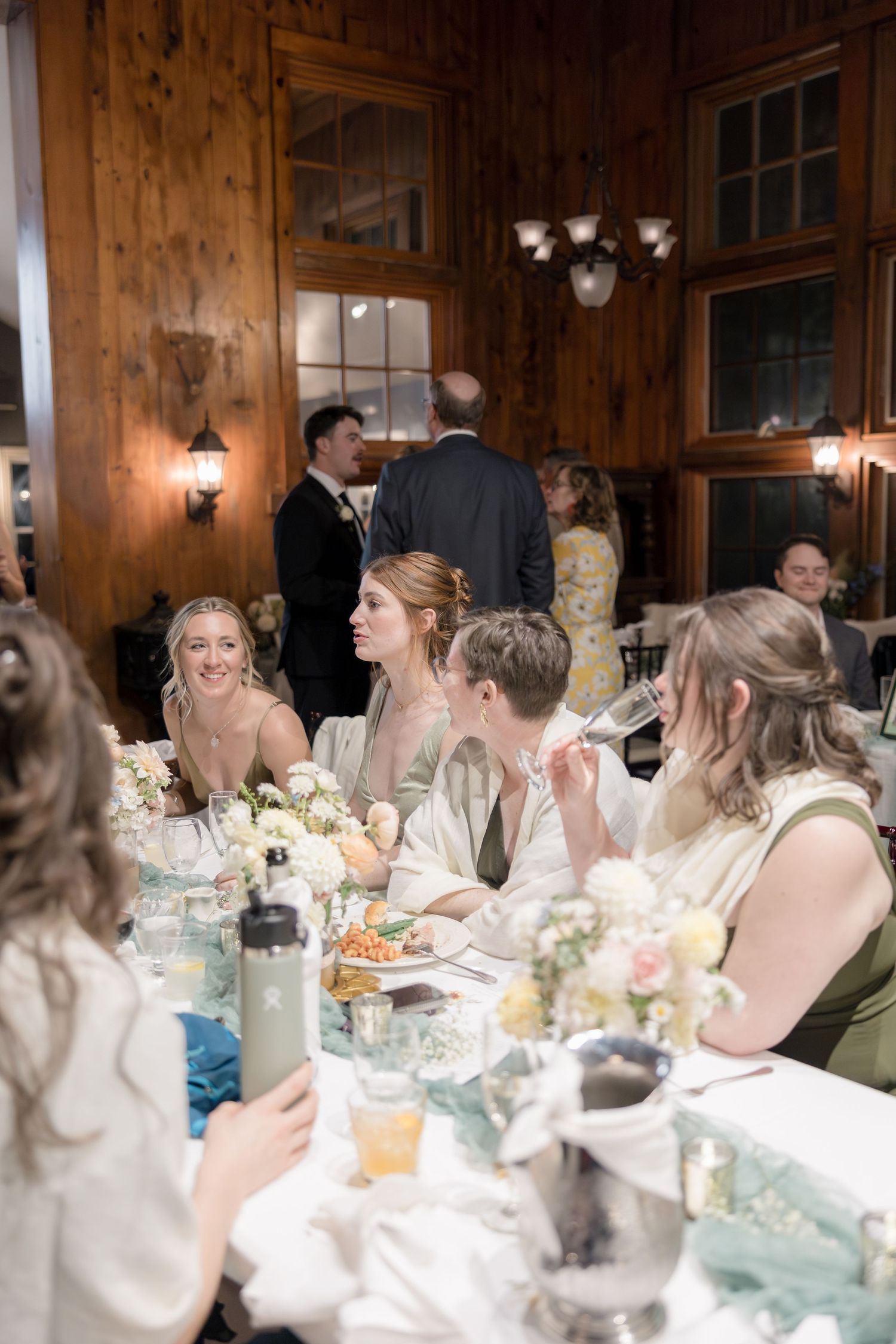 Wedding reception dining scene in rustic wood-paneled room with warm lighting and table settings.