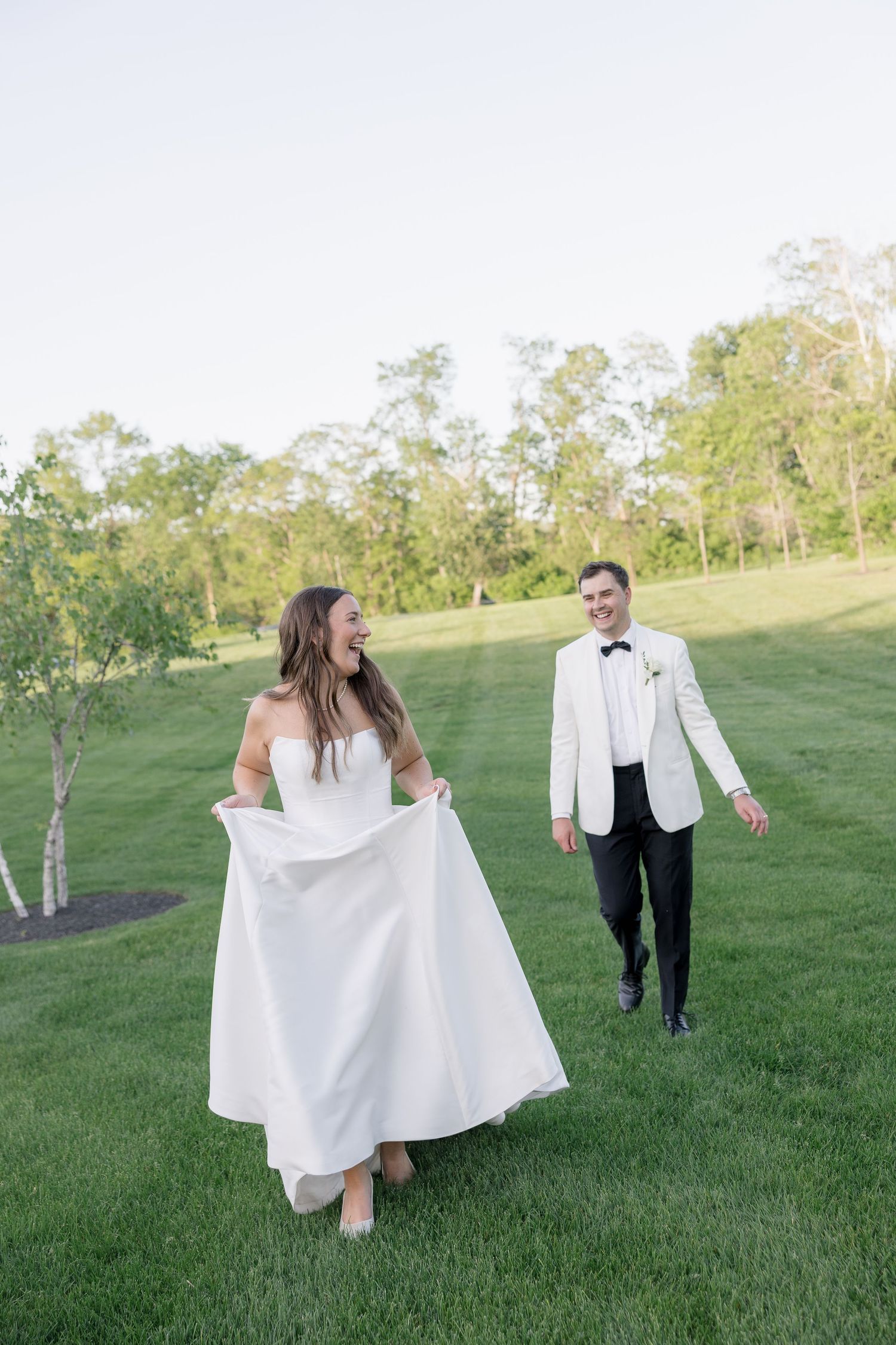 Joyful bride lifts her white gown while laughing as the groom in a white tuxedo jacket walks behind her.