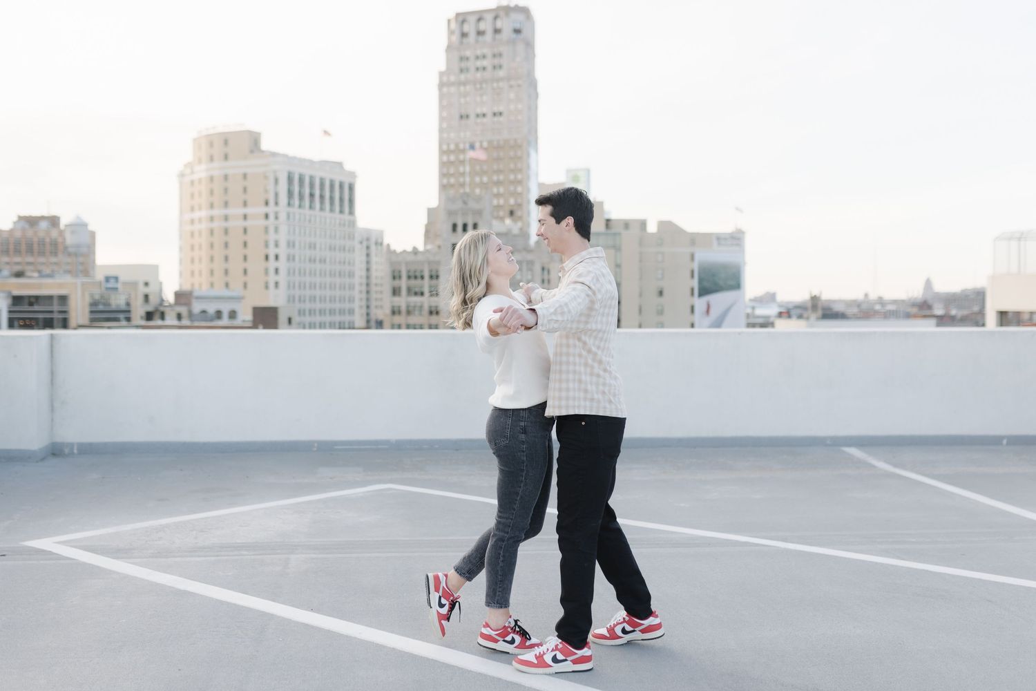 A couple dancing together on an empty rooftop parking lot with city buildings in the background.