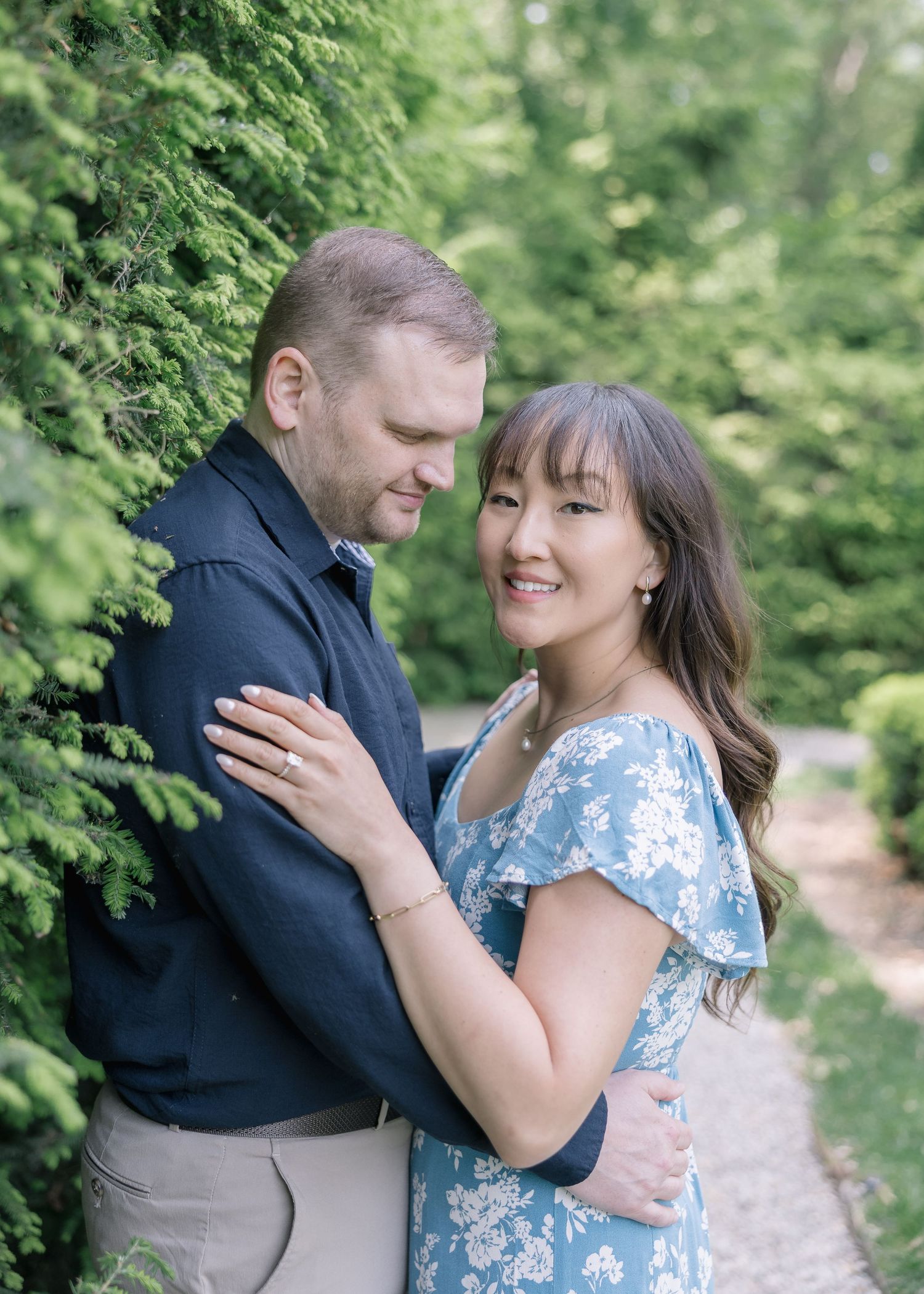 A romantic couple embraces in a lush green park setting wearing blue and navy coordinated outfits.