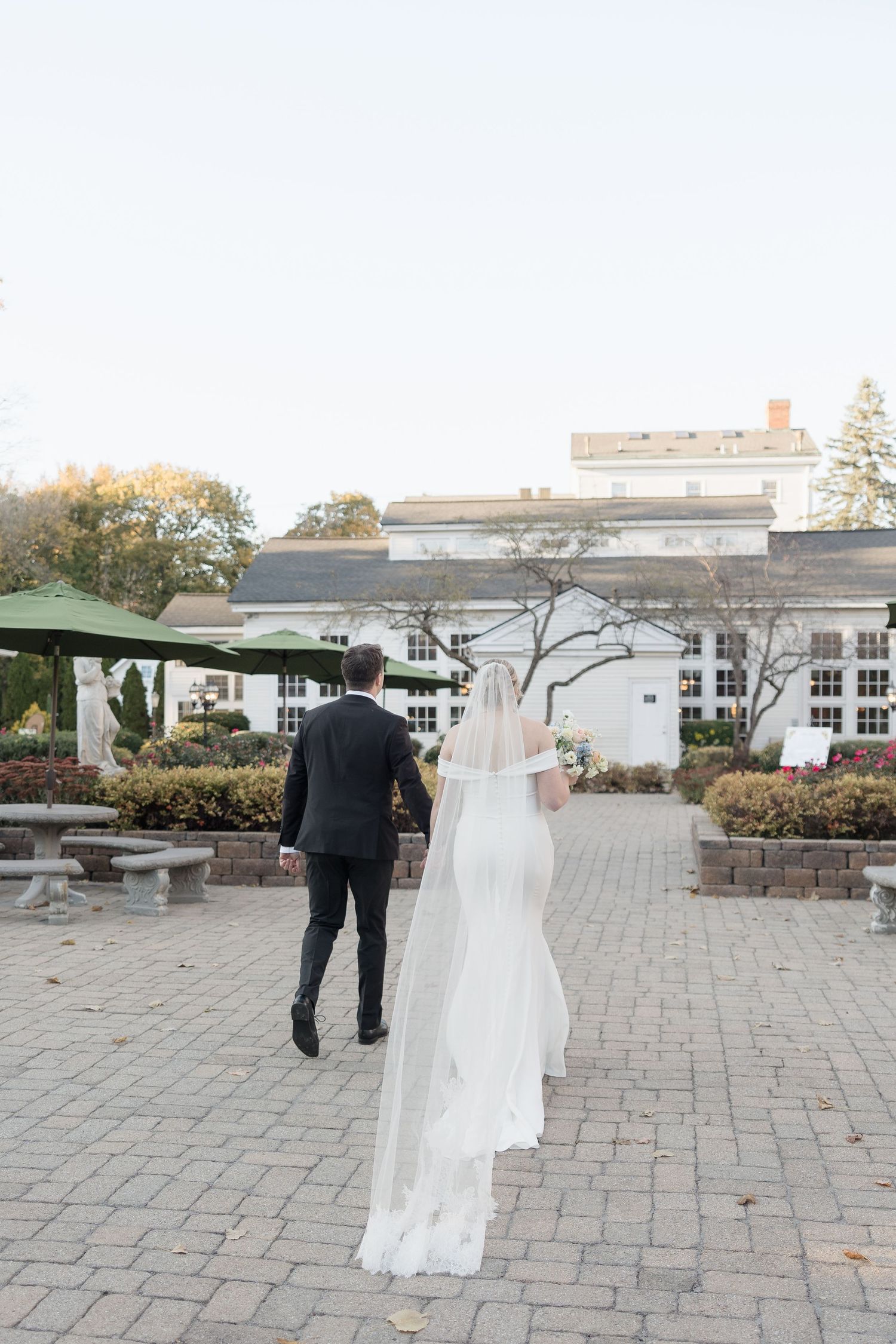 A wedding dress trailing behind on a stone path leading to a white building.