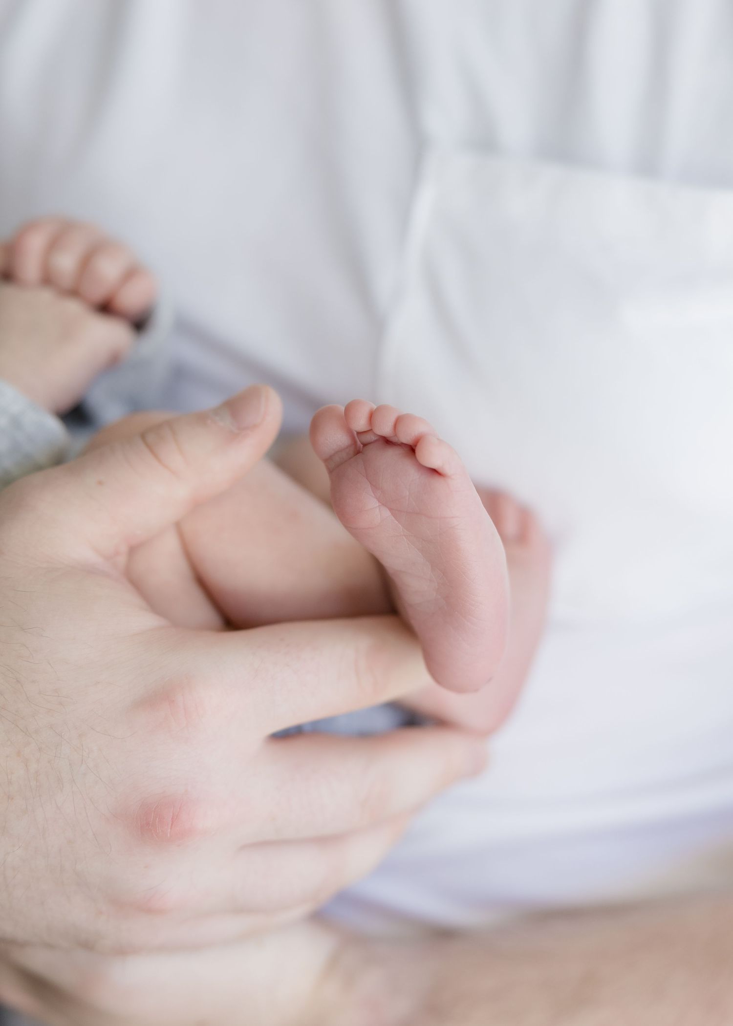 Close-up view of tiny baby feet being gently held by adult hands against white bedding.