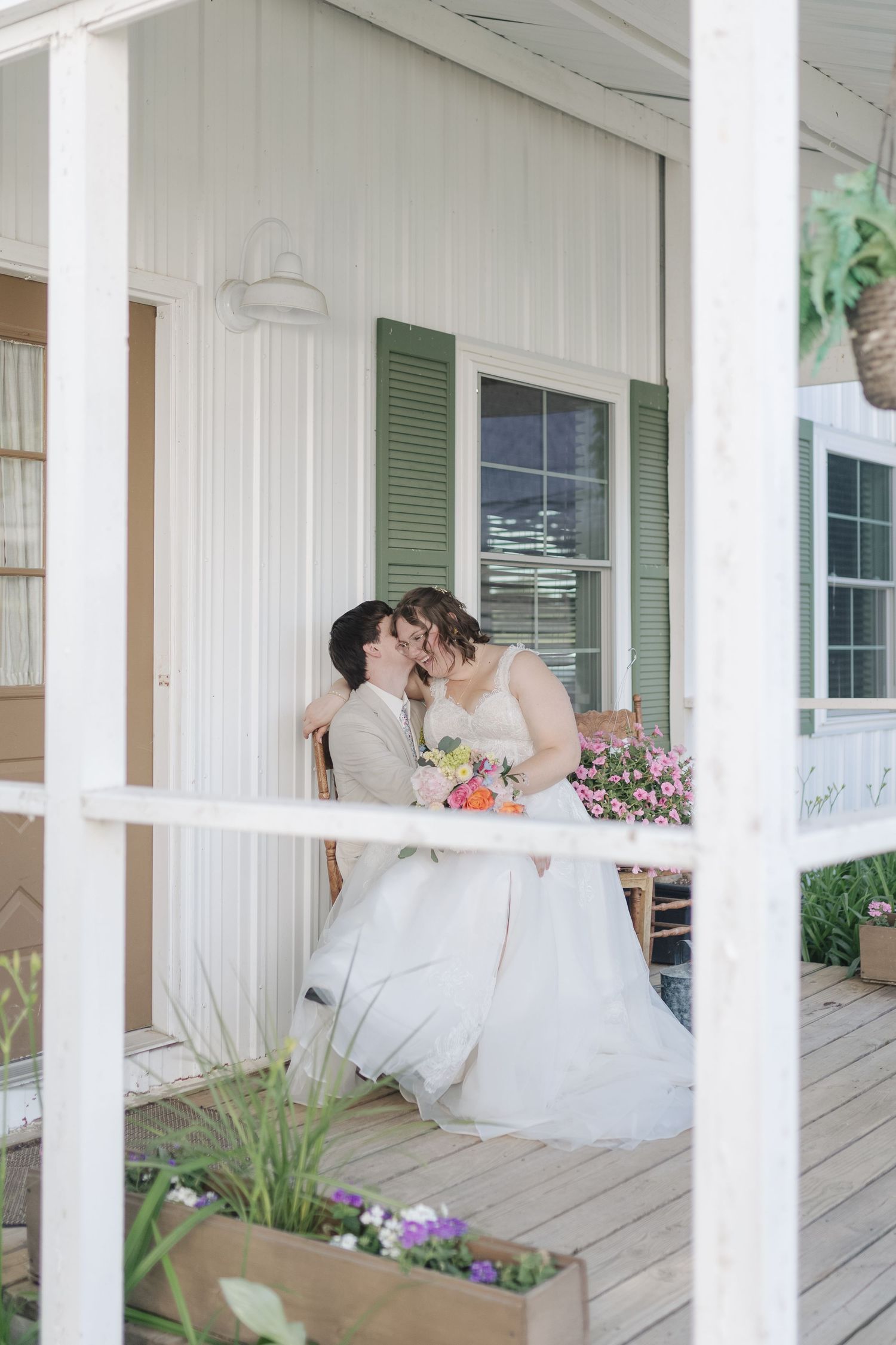 Wedding couple shares romantic moments on a white porch with green shutters.
