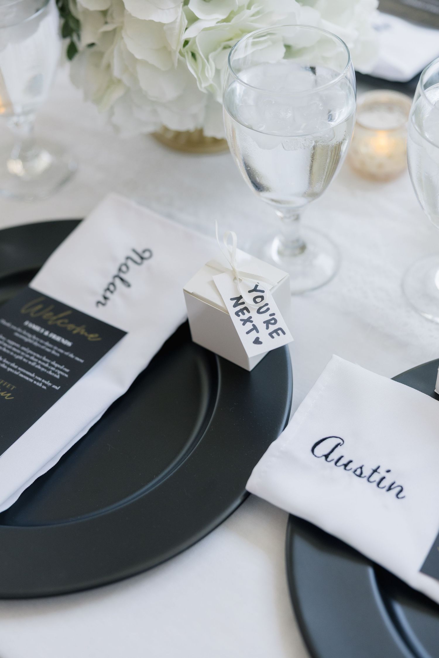 Elegant black and white wedding place setting with personalized napkin, charger plate, and favor box.