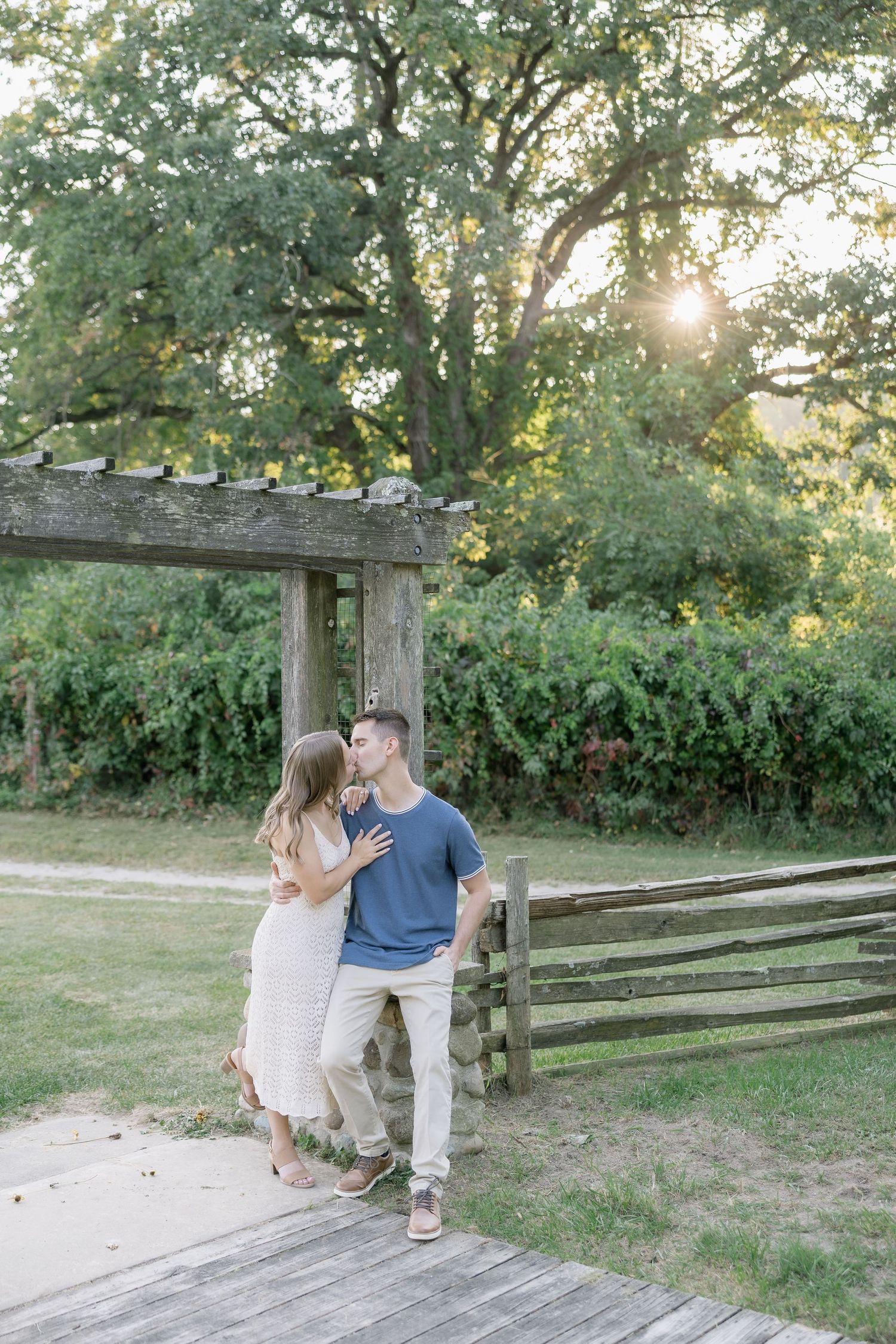 A couple sits together on a rustic wooden fence at sunset in a natural outdoor setting.