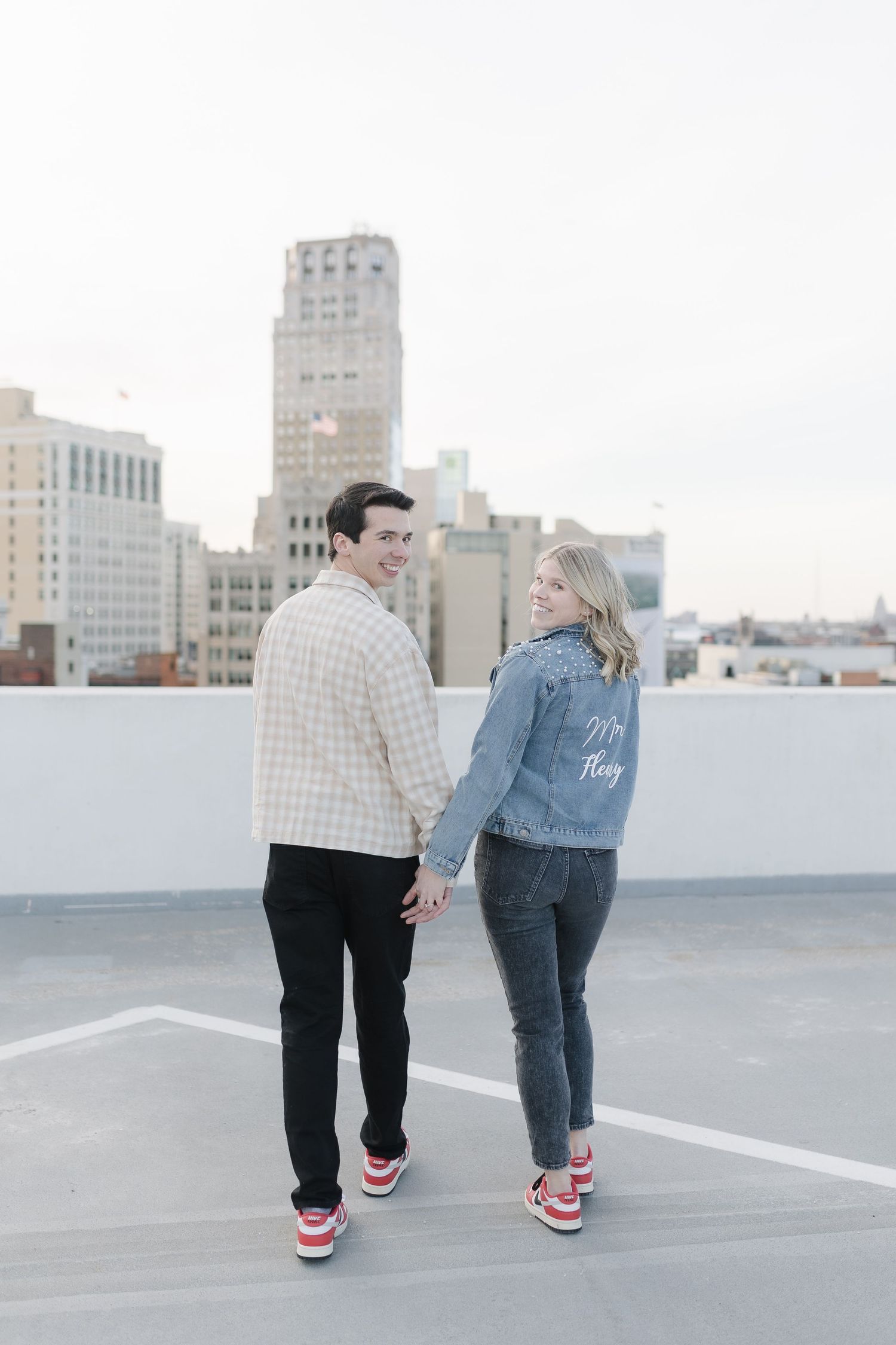 Couple wearing matching sneakers walking hand in hand on a downtown rooftop.