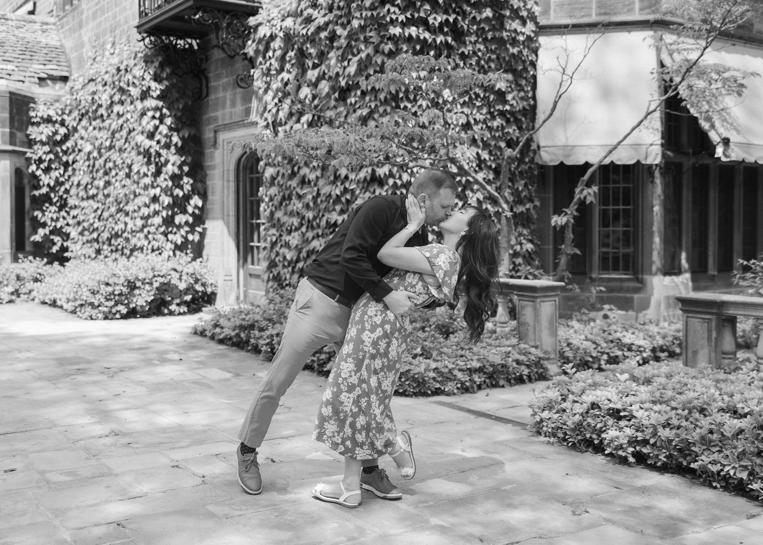 A playful couple dances and twirls together on a stone patio surrounded by ivy-covered walls.