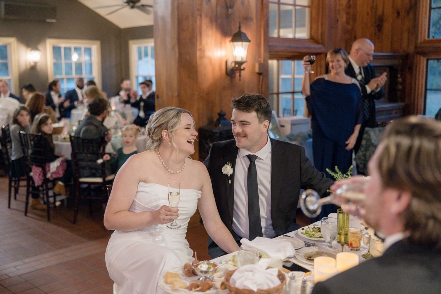Couple sharing a candid moment during their wedding reception at a rustic wooden-paneled venue.