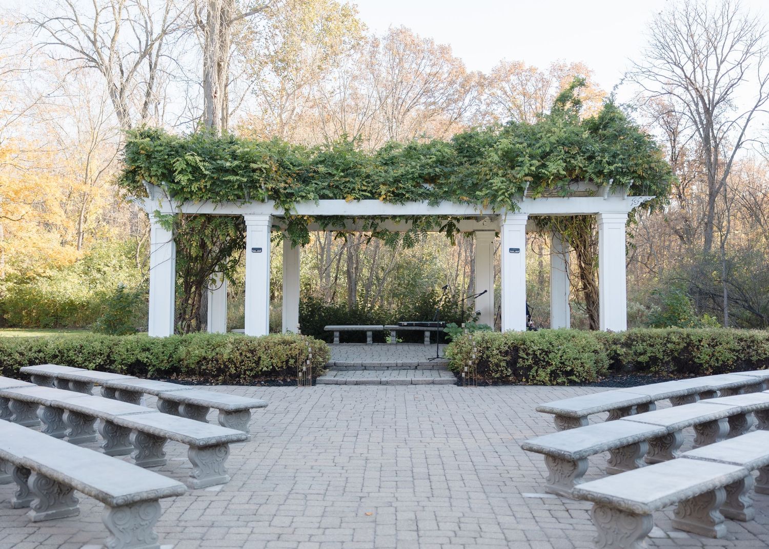 Outdoor garden ceremony space with white pillars, stone benches, and ivy-covered pergola.