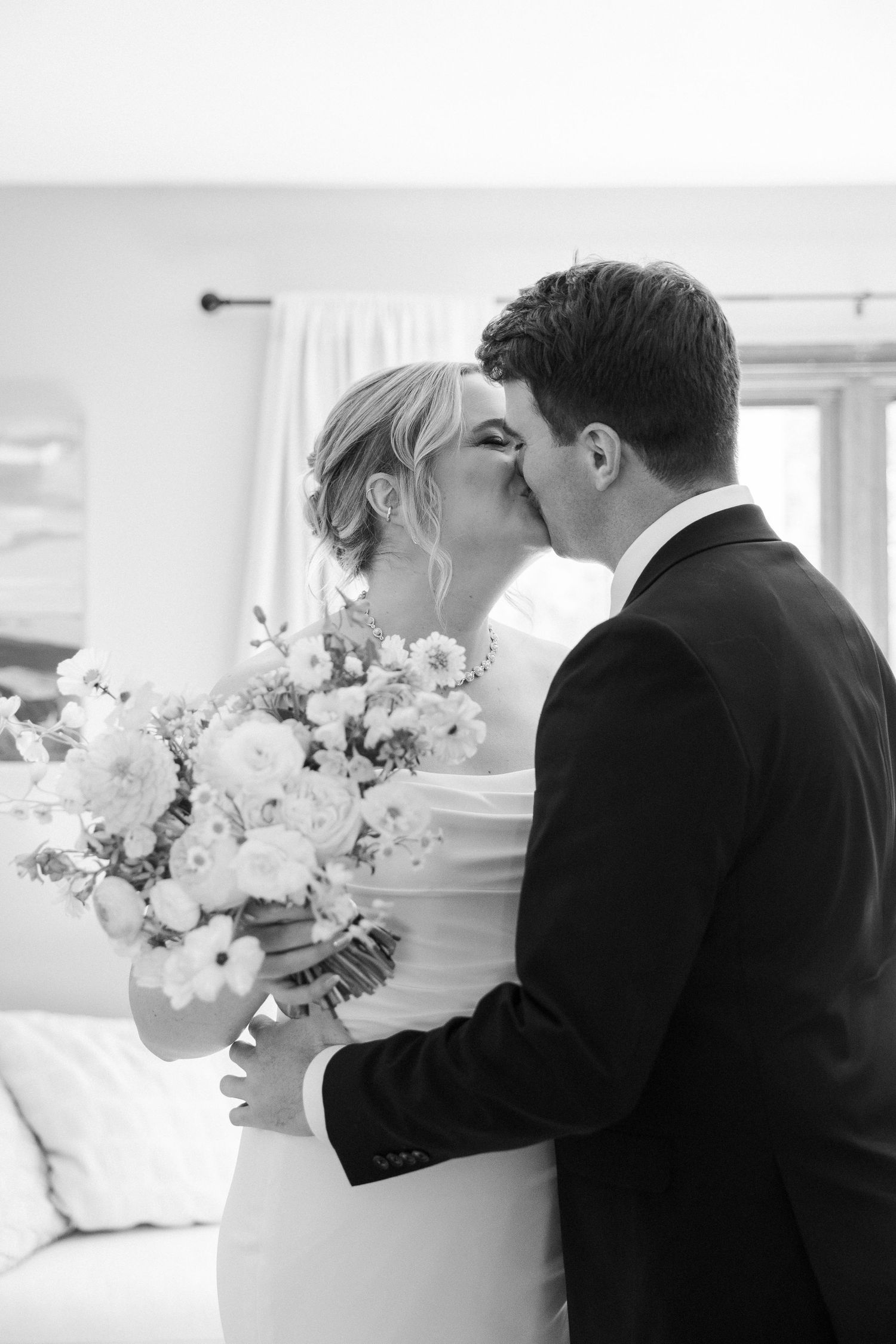 A romantic black and white wedding photo capturing a tender kiss between the bride and groom with a bouquet of flowers.