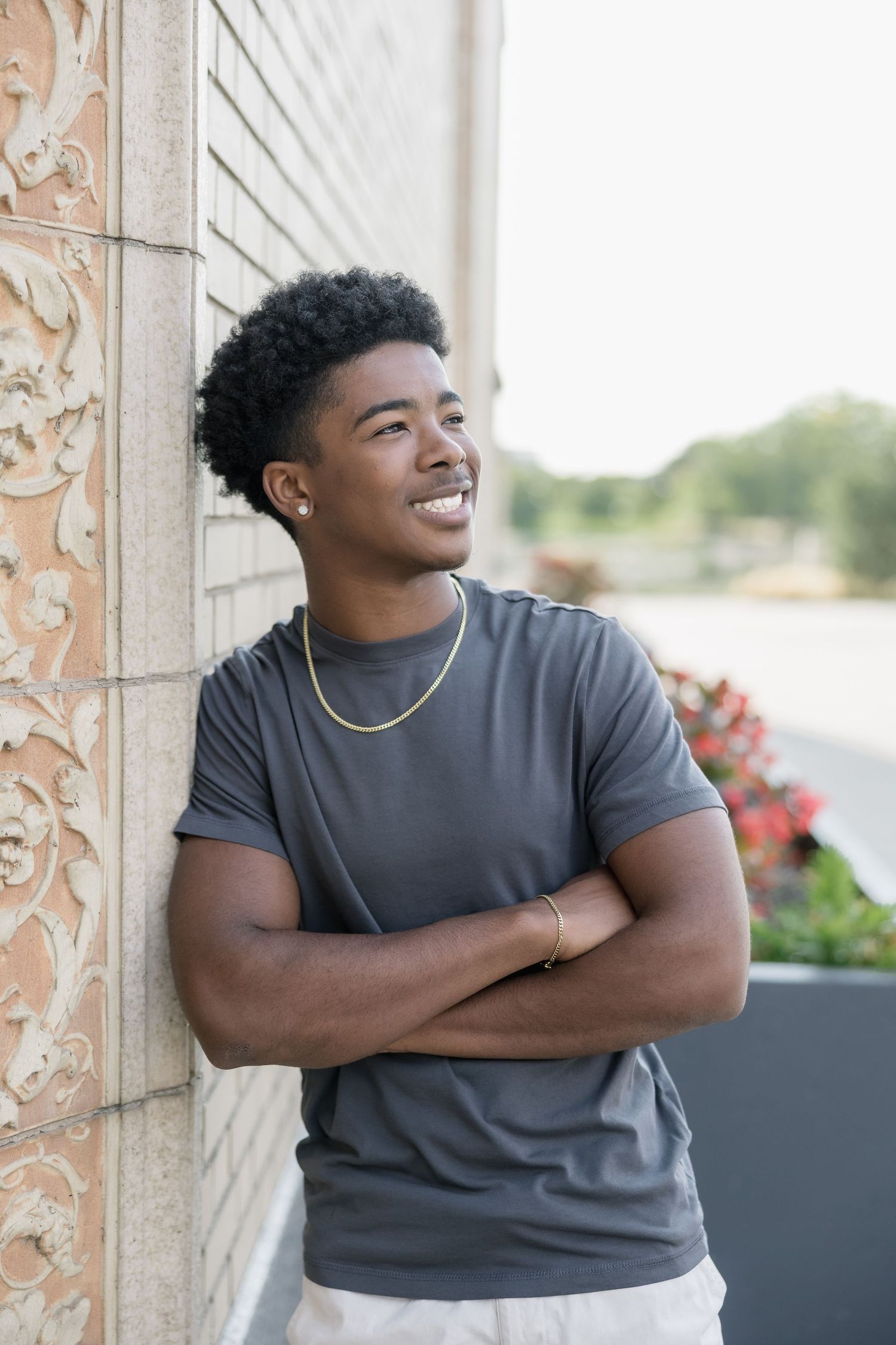 Someone in a dark gray t-shirt poses against a light-colored wall while looking up and smiling.