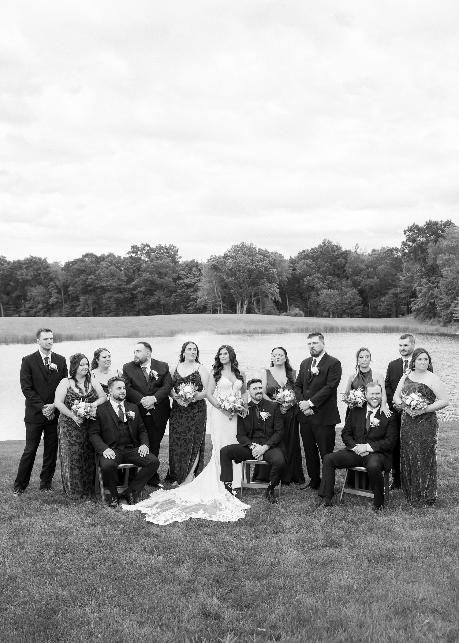 Wedding party in black and white attire posed together in grassy field.