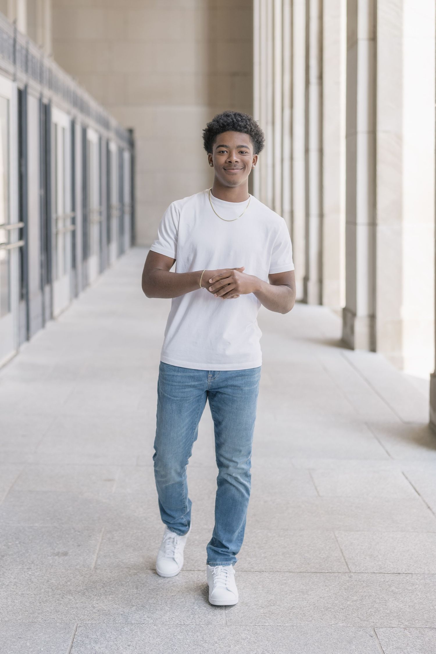 Person wearing white t-shirt and blue jeans walking through bright corridor with columns.