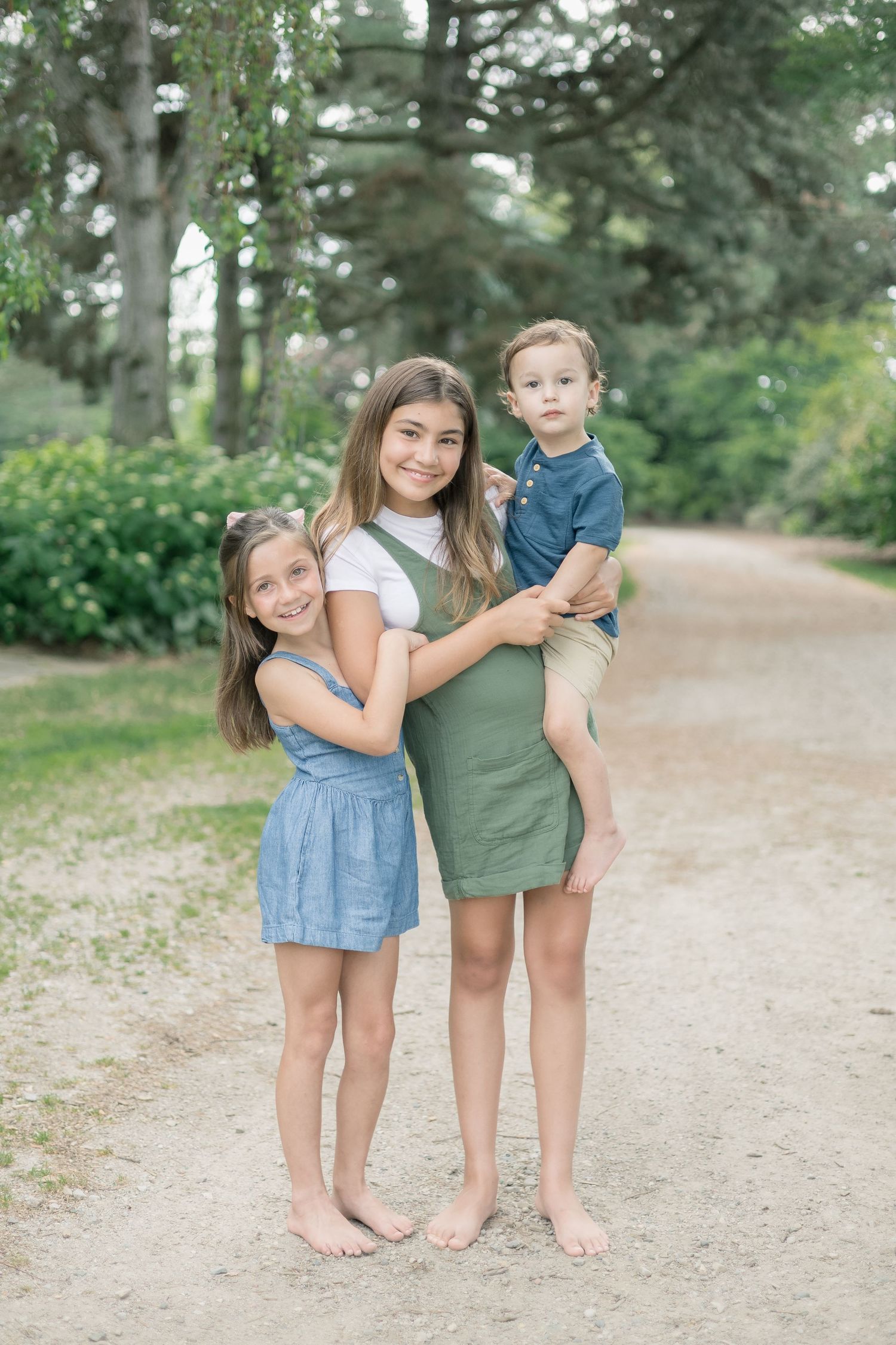 A family in casual clothing poses together on a dirt path surrounded by evergreen trees in a park setting.