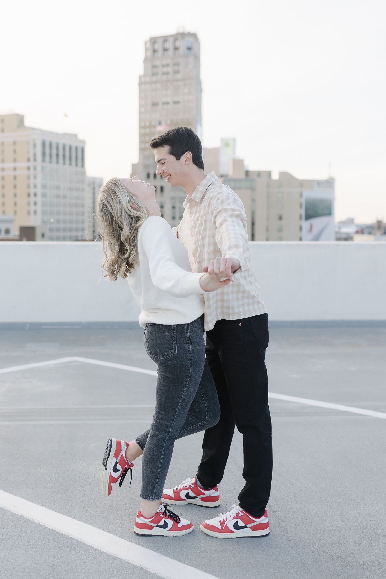 Couple in coordinated outfits dancing together on a city rooftop parking area.
