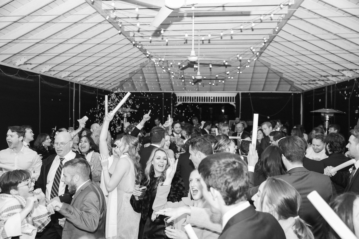 Black and white photograph of a crowded dance floor with people dancing with their arms raised.