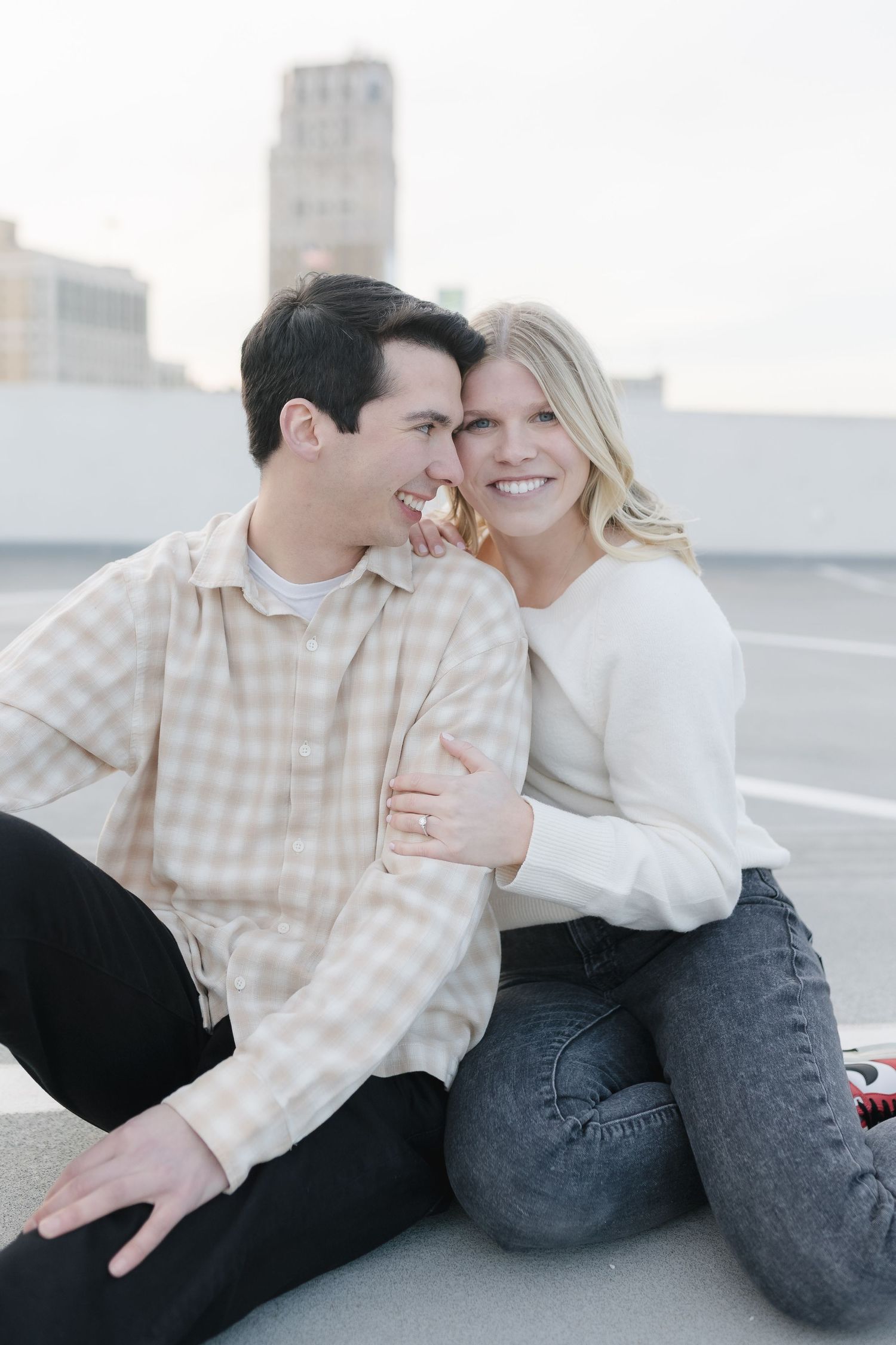 An intimate moment captured between a couple sitting together on a rooftop with urban scenery behind them.